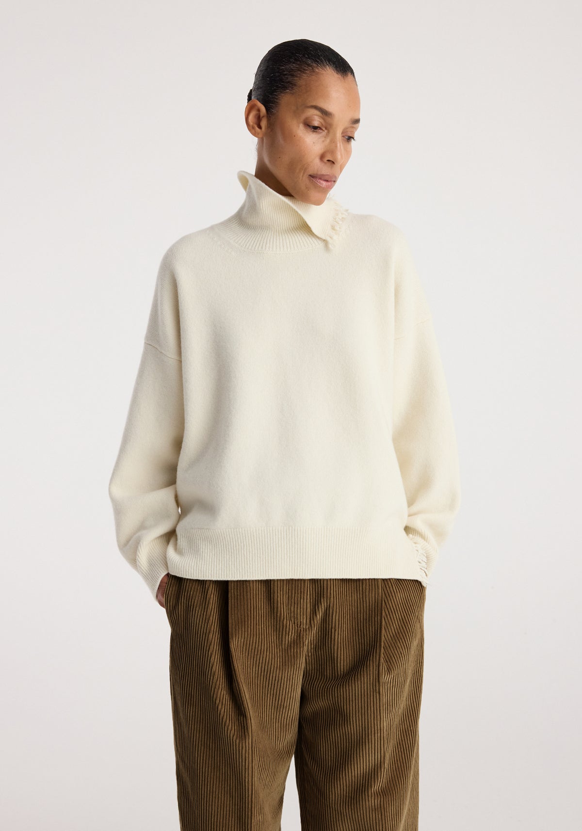 Woman wearing a Turtleneck with raw details | off white sweater with a high collar and loose sleeves paired with brown corduroy pants.