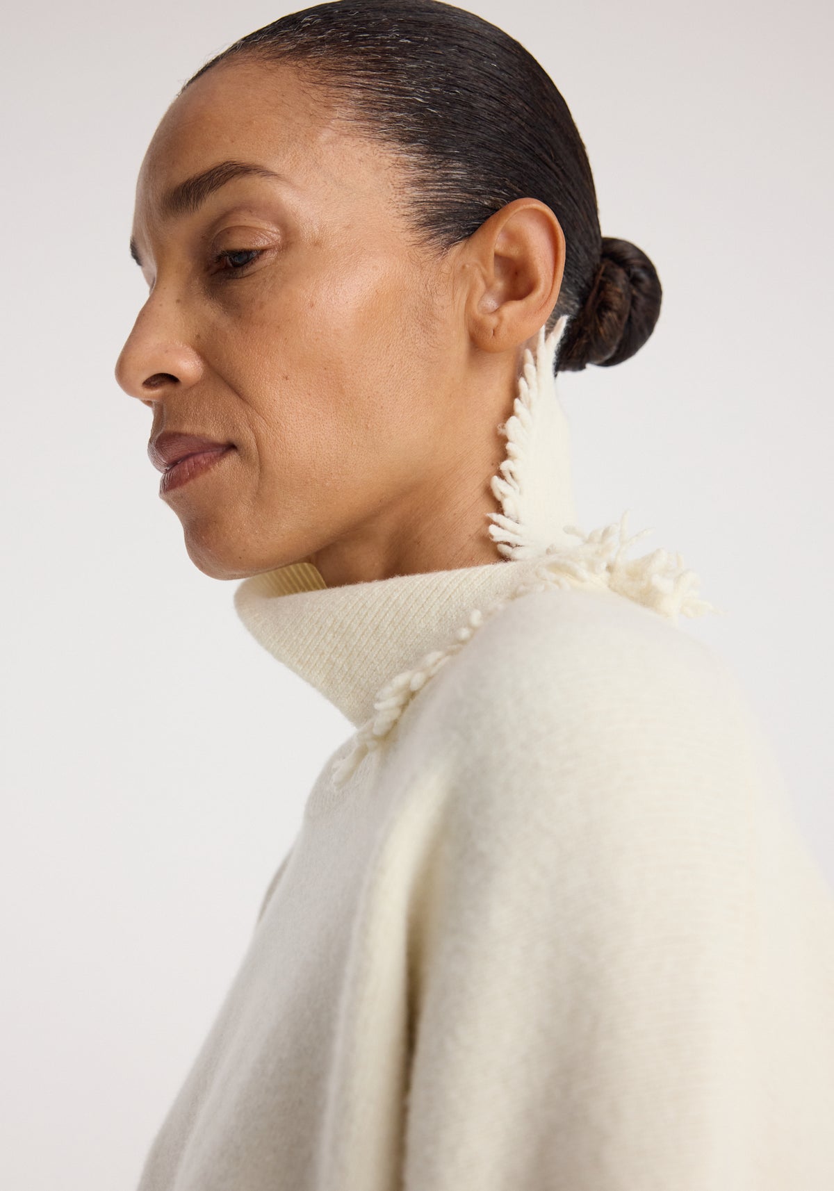 Close-up side view of a woman wearing a Turtleneck with raw details | off white, featuring a high neck with textured raw edges and a soft knit fabric.
