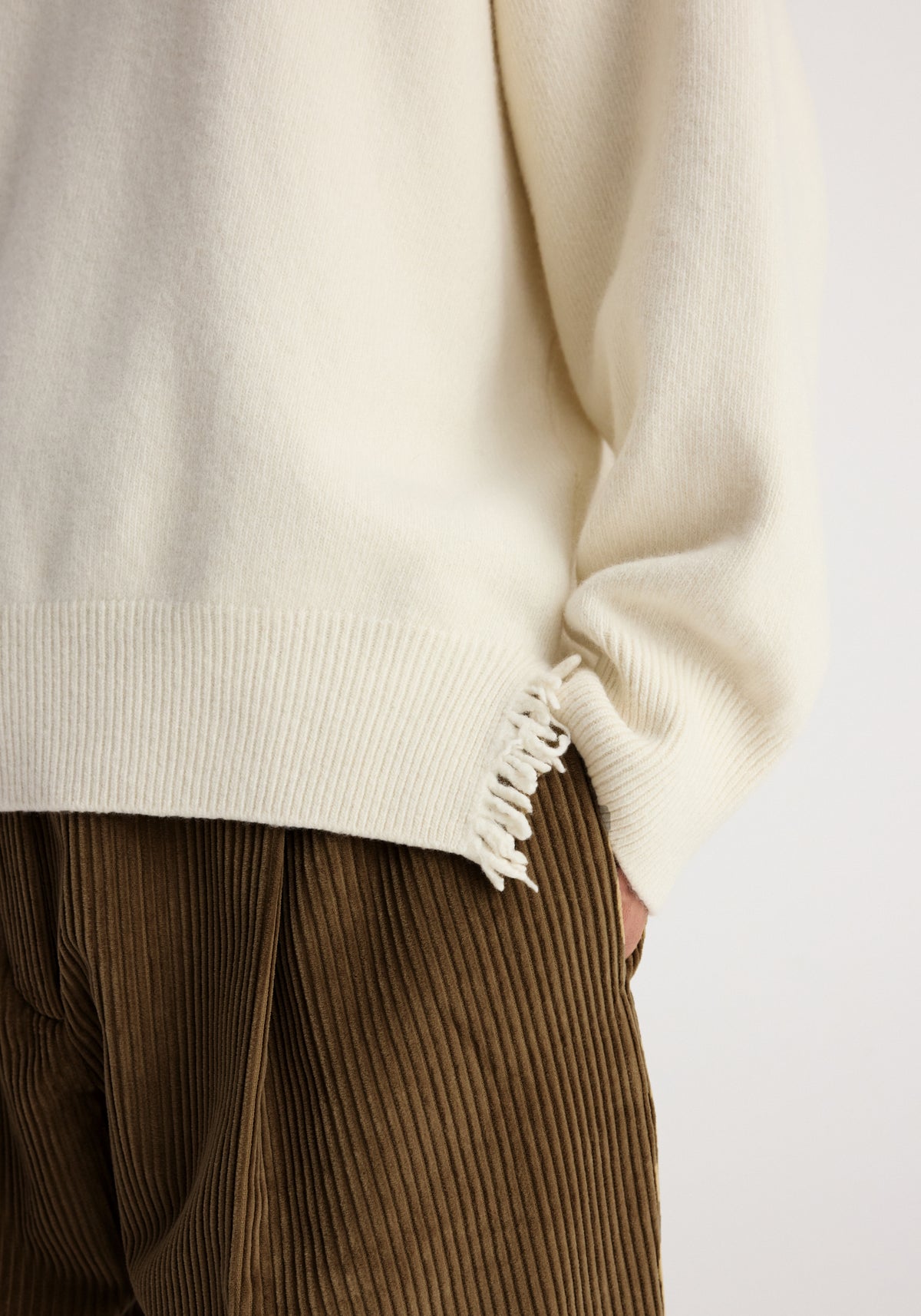 Close-up of the hem and sleeve of the Turtleneck with raw details | off white, showcasing the textured knit fabric and frayed edge design detail.