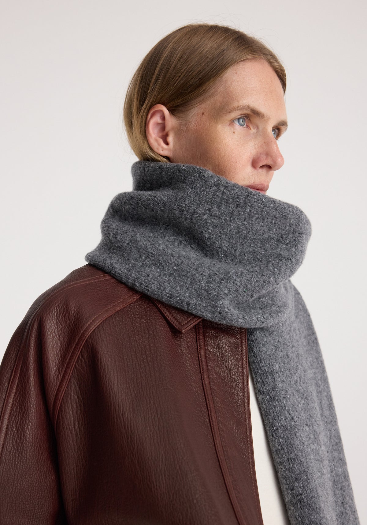 Close-up of a person wearing a thick, soft gray knitted mouliné scarf | anthracite melange wrapped around the neck, paired with a dark brown leather jacket.