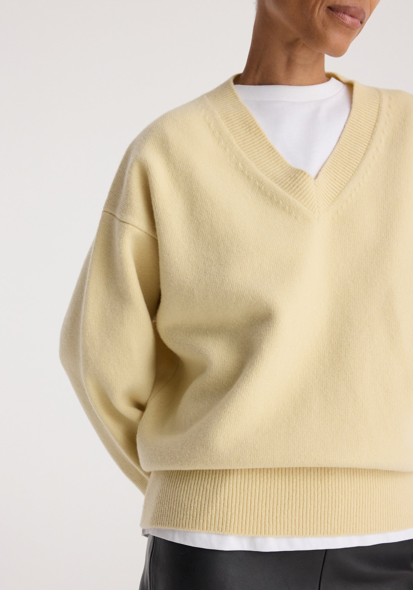 Close-up of a person wearing a soft, butter-colored Classic v-neck jumper | butter layered over a white shirt with ribbed cuffs and hem.