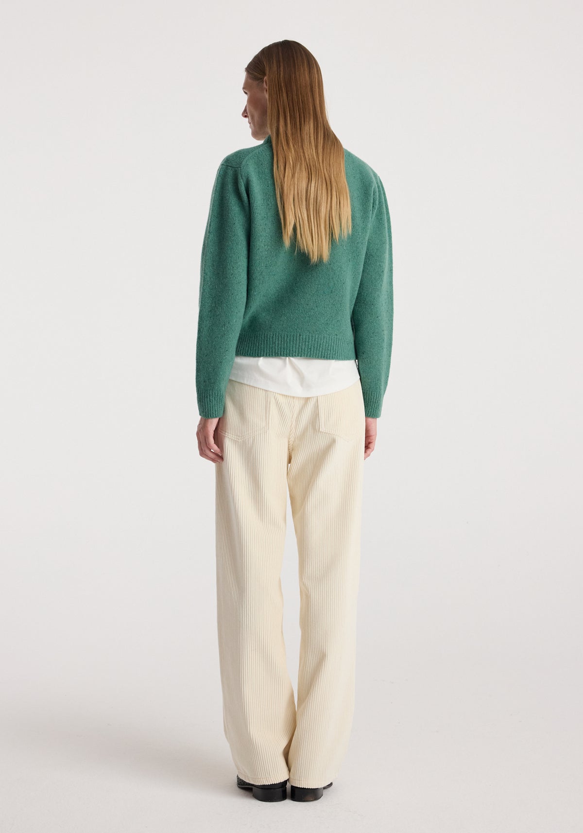Back view of a model wearing the Fitted mouliné crewneck | jade mouliné in green with cream trousers and black shoes against a neutral studio background