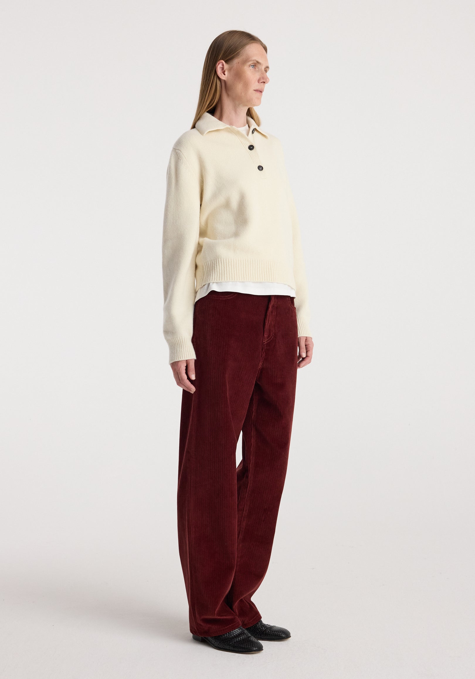 Woman wearing Bruun - Signature baggy corduroy trousers | wine paired with a cream long-sleeve sweater and black shoes, standing against a plain backdrop.