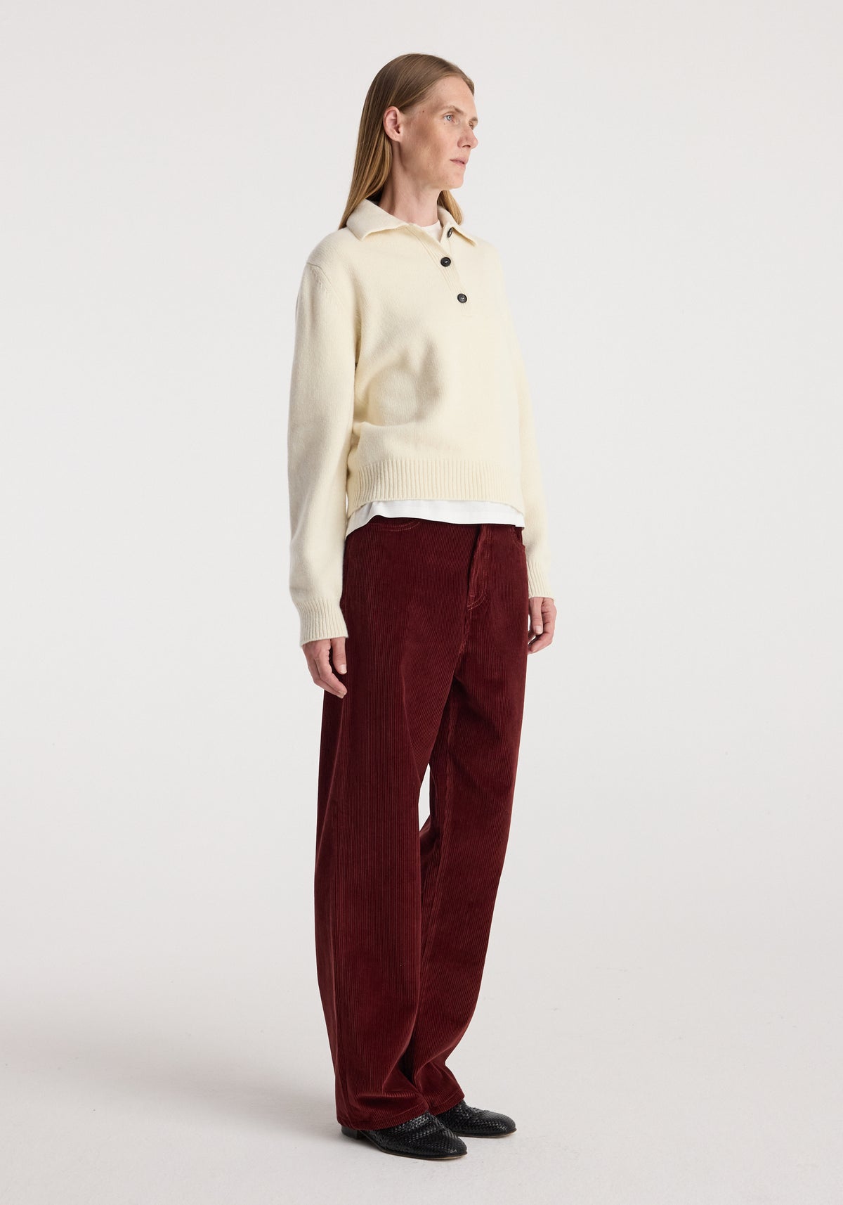Woman wearing Bruun - Signature baggy corduroy trousers | wine paired with a cream long-sleeve sweater and black shoes, standing against a plain backdrop.
