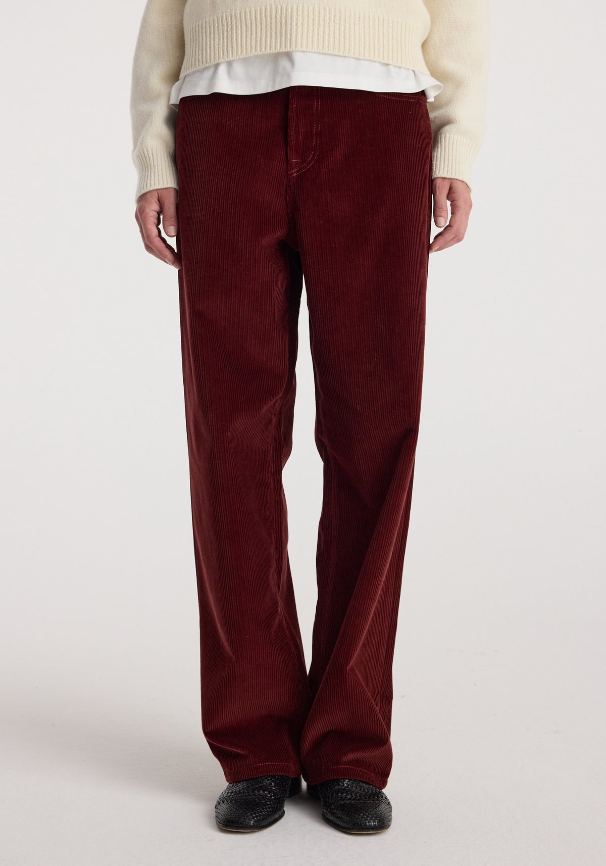 Front view of a person wearing Bruun - Signature baggy corduroy trousers | wine in a deep red color paired with a cream sweater and black textured shoes against a plain white background.