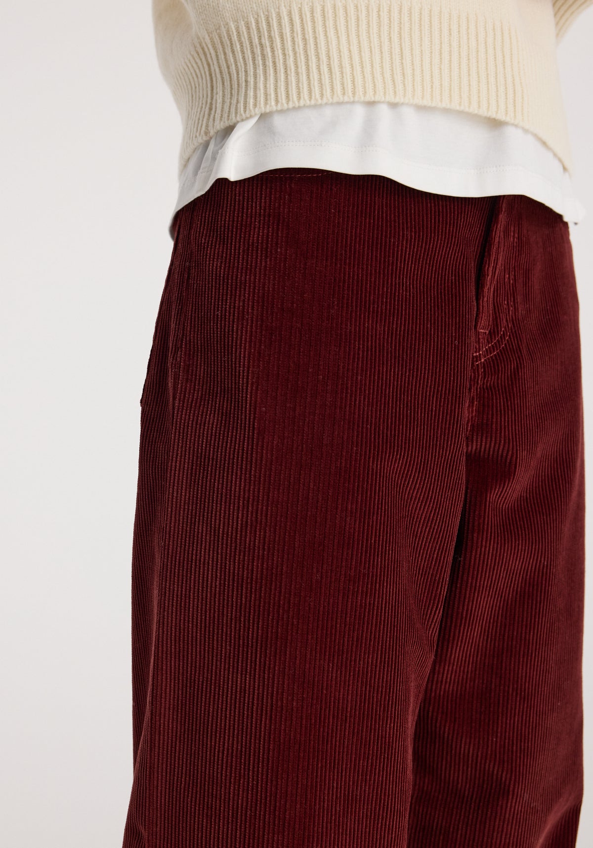 Close-up of wine-colored wide-leg corduroy trousers worn with a cream knit sweater and white shirt, showcasing texture and relaxed fit in Bruun - Signature baggy corduroy trousers | wine.