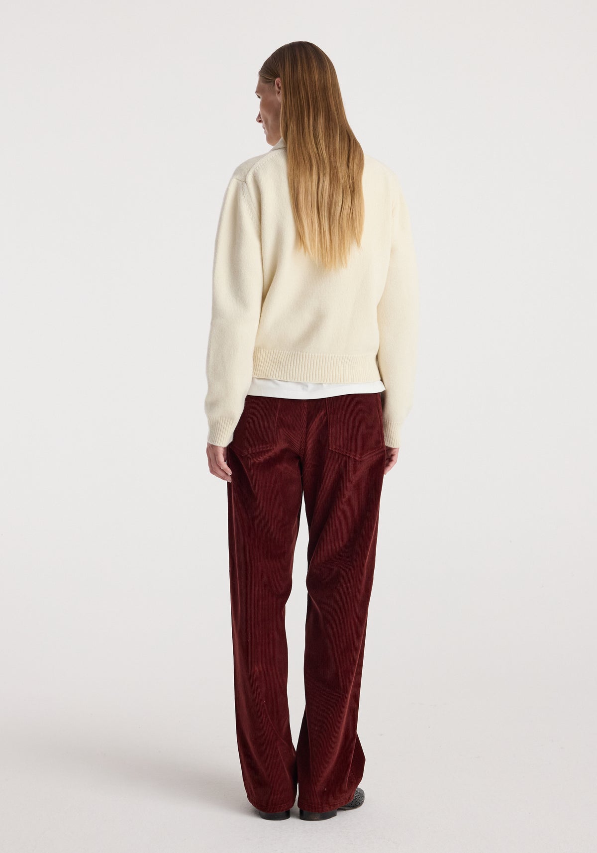 Woman wearing Bruun - Signature baggy corduroy trousers | wine, shown from the back with a cream sweater and black shoes in a studio setting.