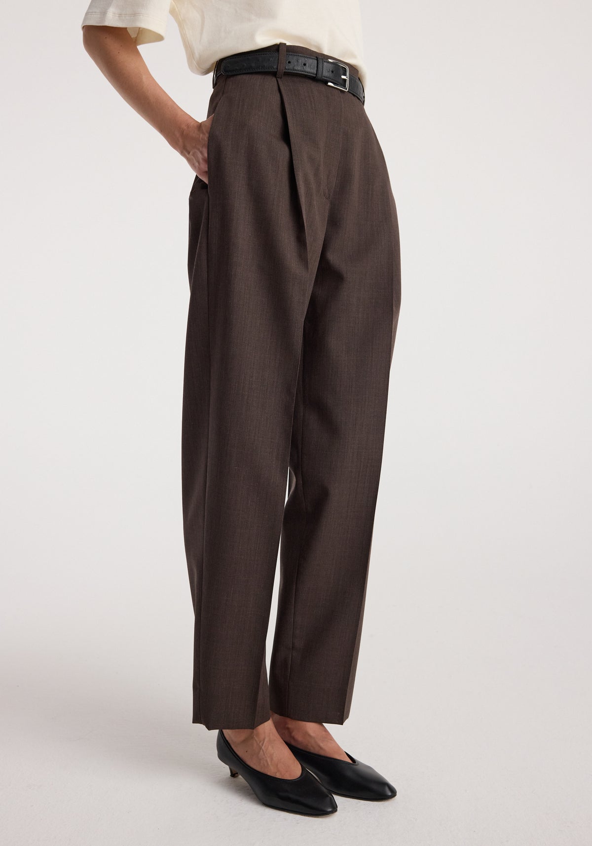 Daria - Single pleat straight leg trousers | dark brown worn with a black belt and pointed black flats, showing the high waist and straight leg fit