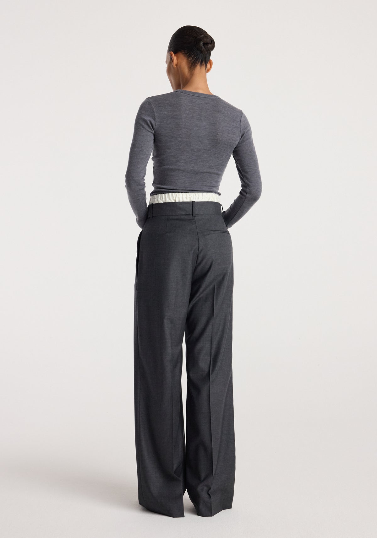 Rear view of a woman wearing Boxer detailed trousers | dark grey melange paired with a fitted long-sleeve top, highlighting the trousers’ tailored fit and wide leg design.