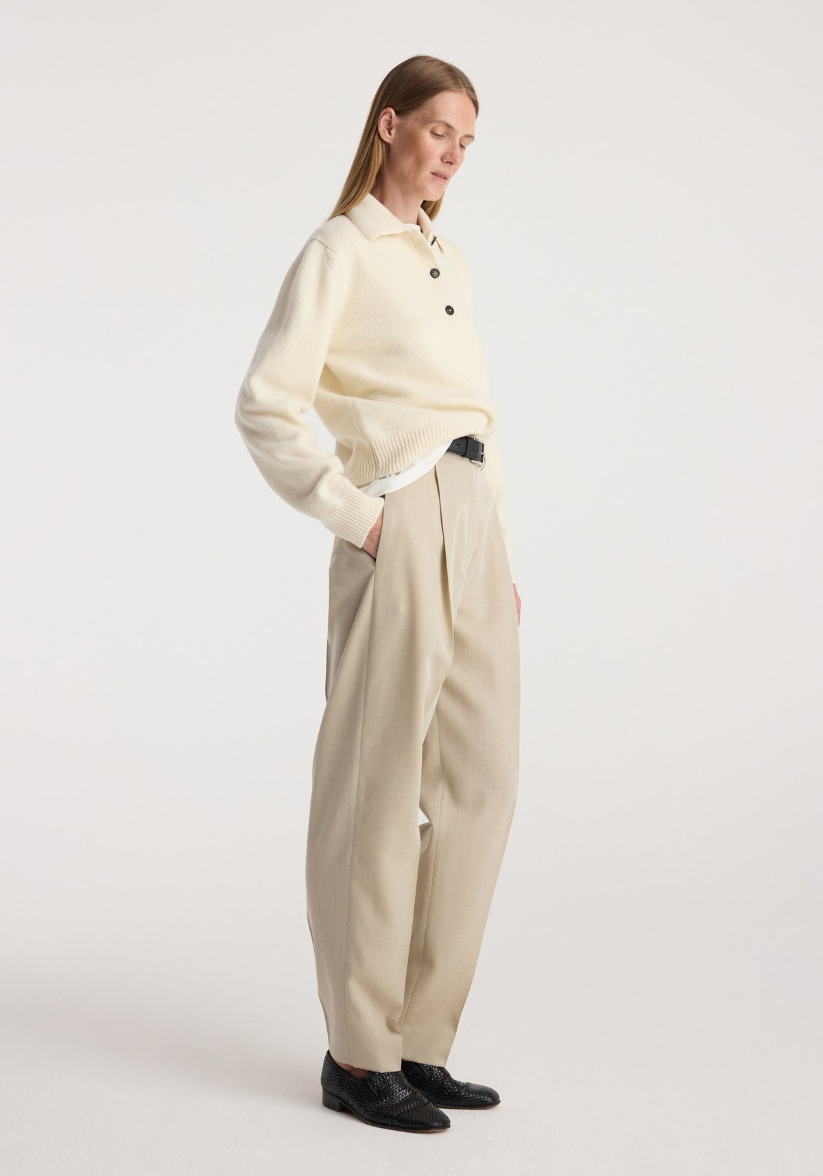 Woman wearing Daria - Single pleat straight leg trousers | butter paired with a cream buttoned sweater and black shoes, standing against a plain background.
