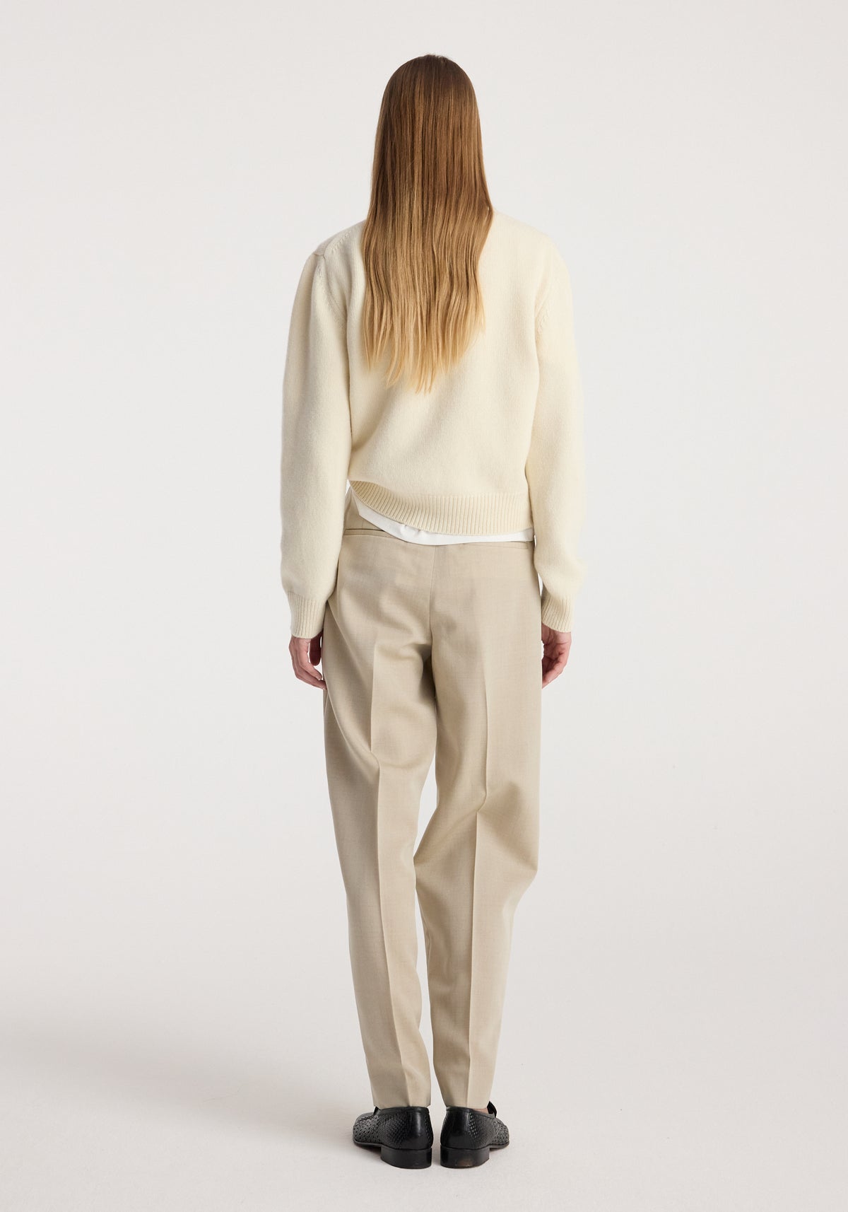 Woman seen from behind wearing Daria - Single pleat straight leg trousers | butter paired with a cream sweater and black shoes against a plain background.