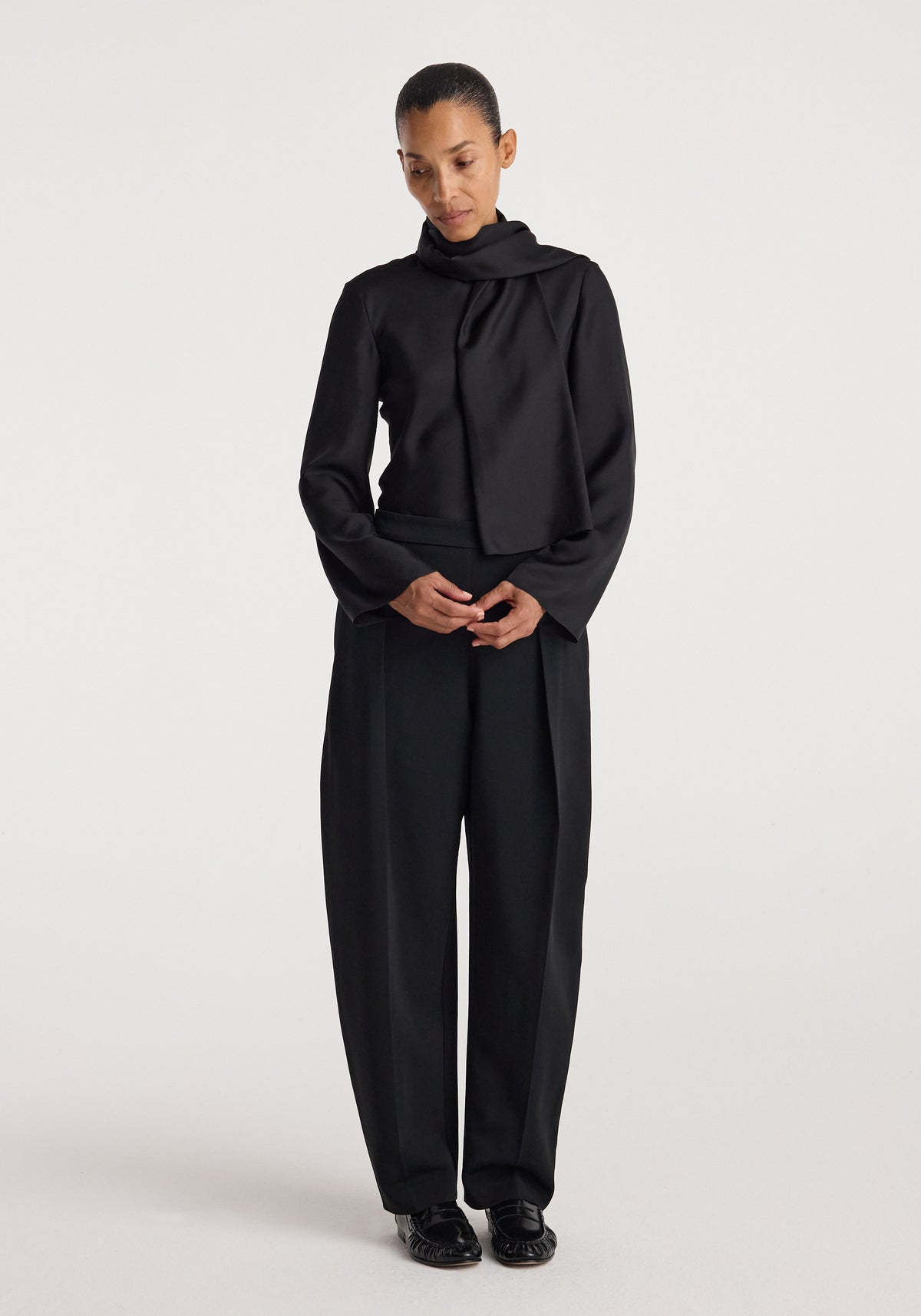 Puck - Sculptural tailored trousers | black worn by a model with a black draped top in a minimalist studio setting
