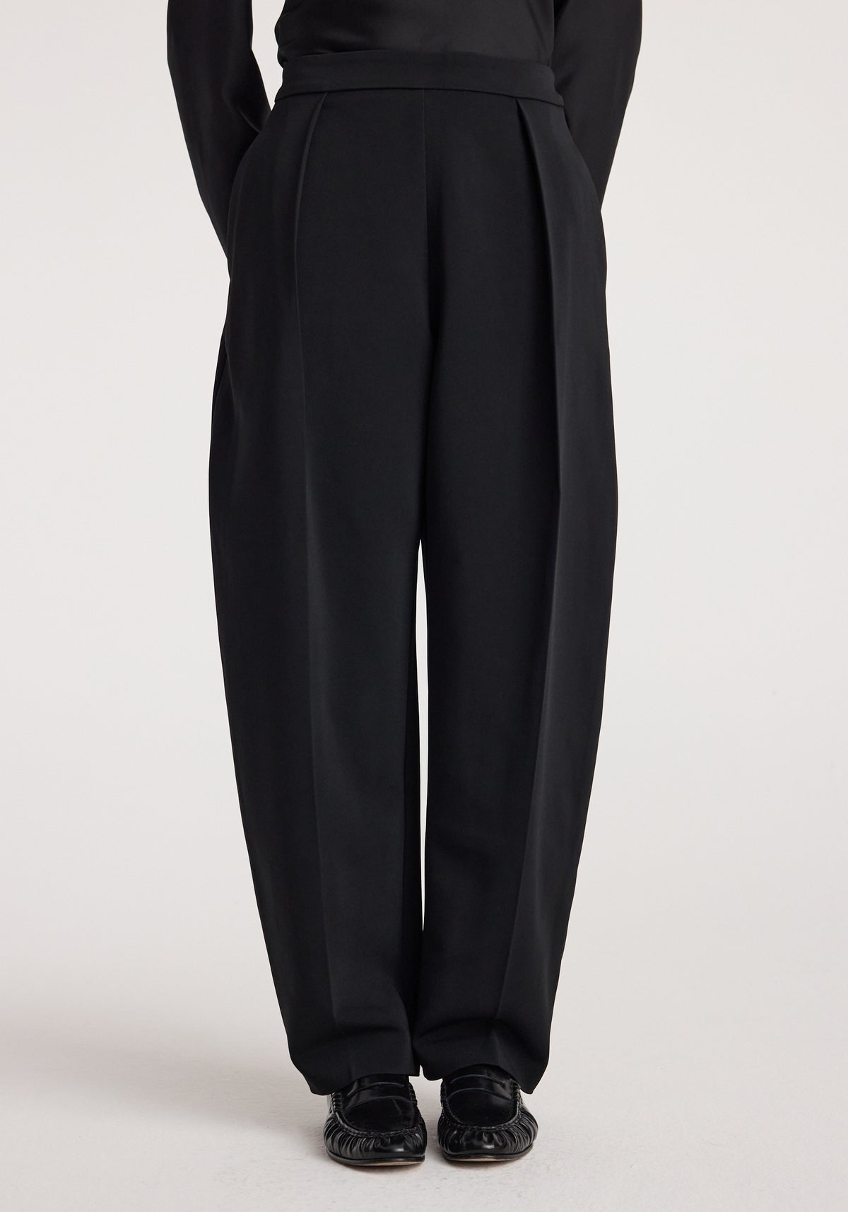 Puck - Sculptural tailored trousers | black, shown on a model with high waist, front pleats, tapered legs, and polished black shoes