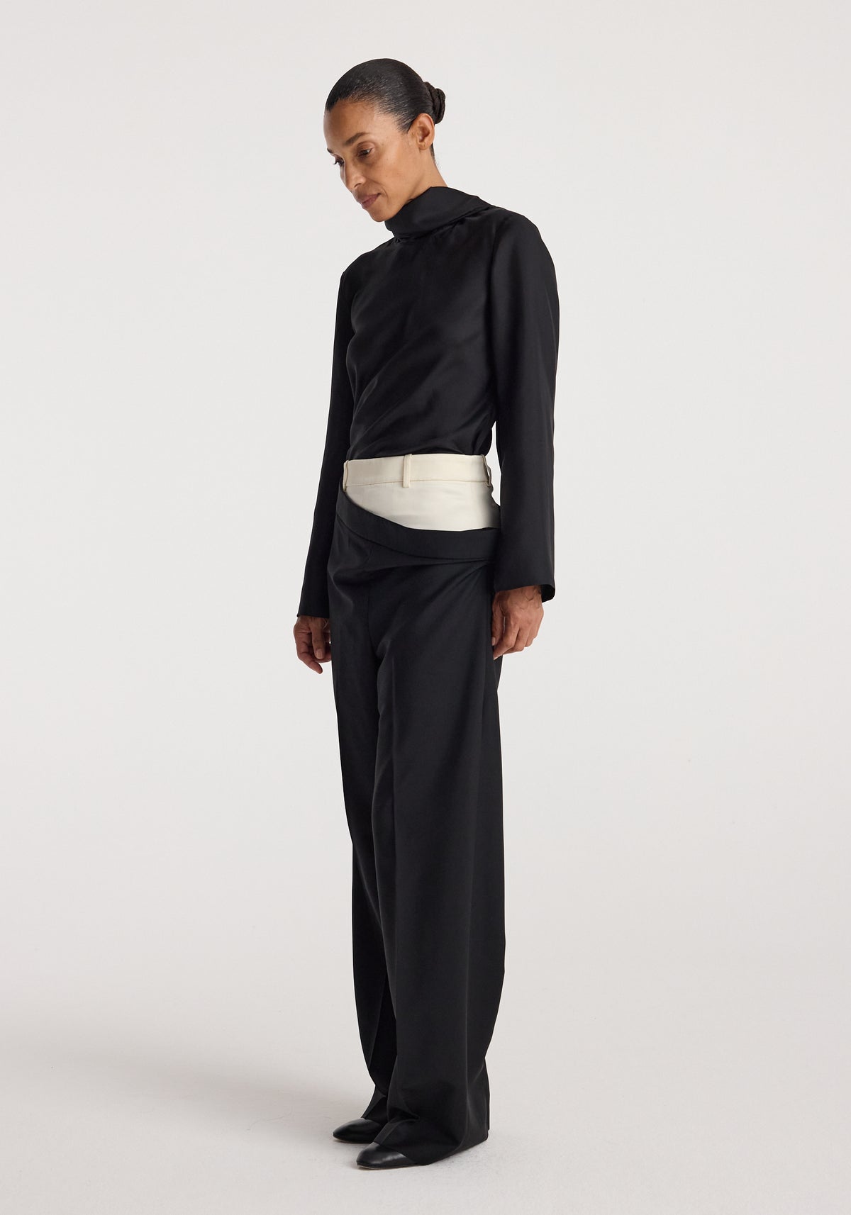Model wearing black Double waistband trousers | black with a contrasting white double waistband detail, paired with a black long-sleeve top and black shoes, standing against a plain white background.