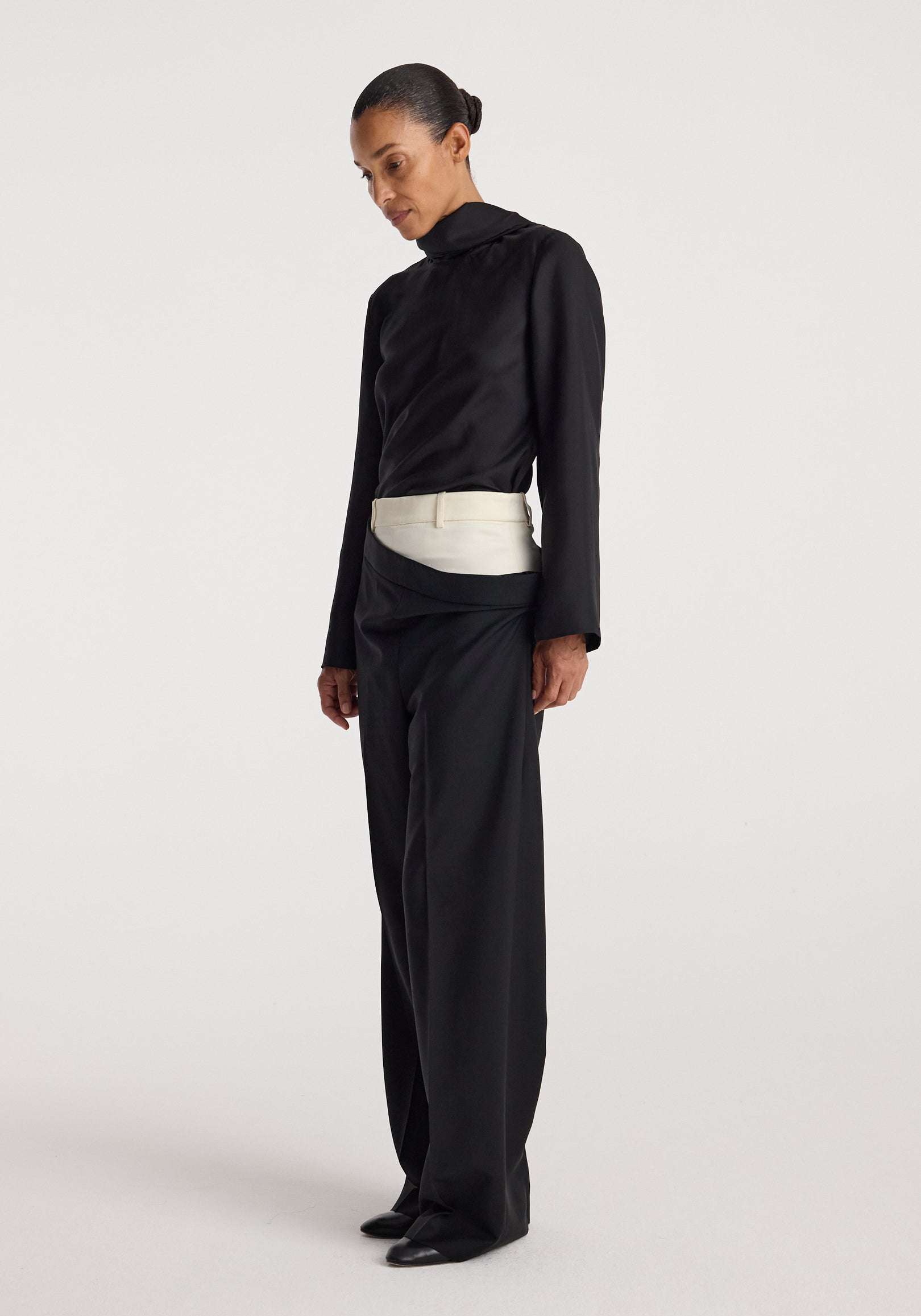 Model wearing black Double waistband trousers | black with a contrasting white double waistband detail, paired with a black long-sleeve top and black shoes, standing against a plain white background.
