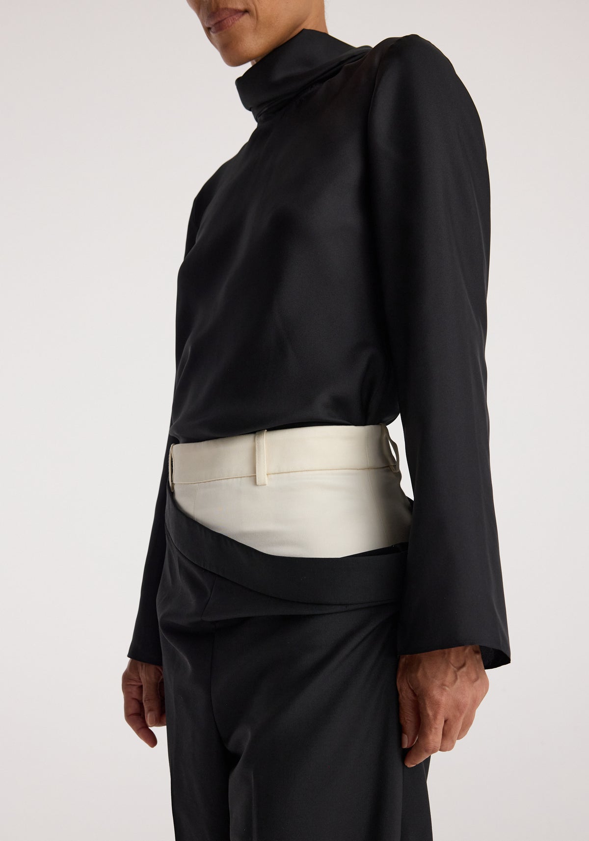 Close-up of a person wearing Double waistband trousers | black, featuring a unique double waistband design with the outer black waistband folded down to reveal a contrasting inner white waistband, paired with a black long-sleeve top.