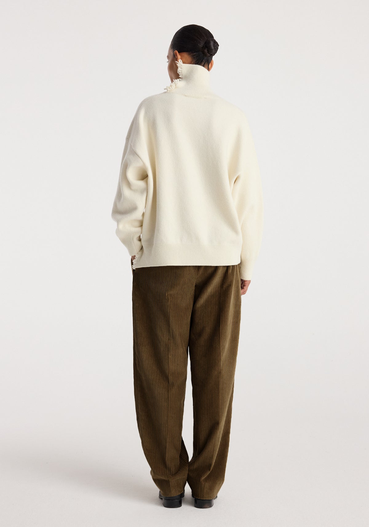 Woman seen from the back wearing Daria - Single pleat straight leg corduroy trousers | caramel paired with a cream-colored oversized sweater.