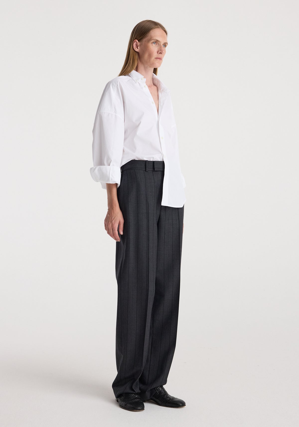 Woman wearing Kee - Straight leg tailored trousers | charcoal stripe with a white button-up shirt and black shoes, standing against a plain light background.