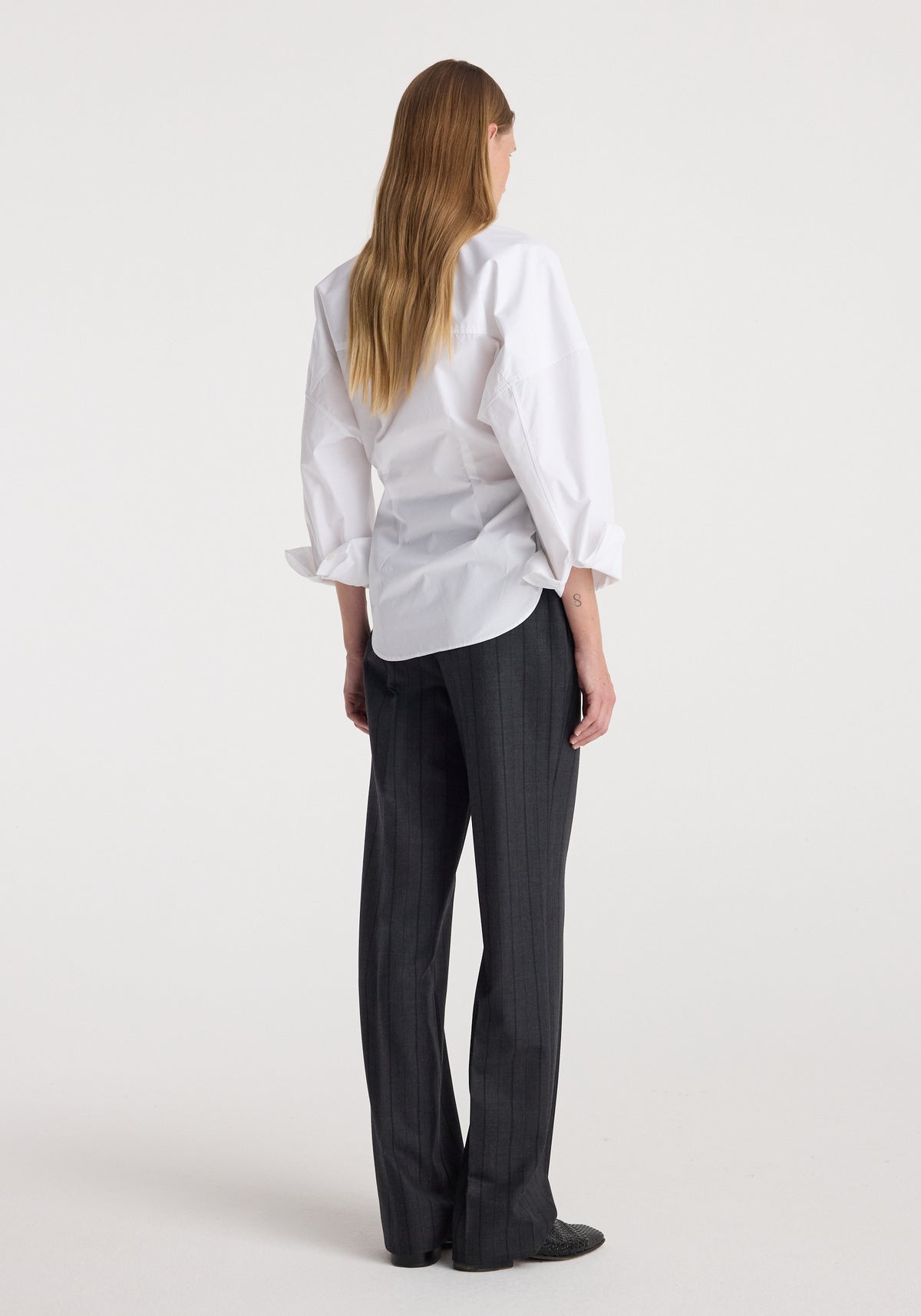 Woman wearing Kee - Straight leg tailored trousers | charcoal stripe paired with a white long-sleeve shirt, standing facing away against a plain background.