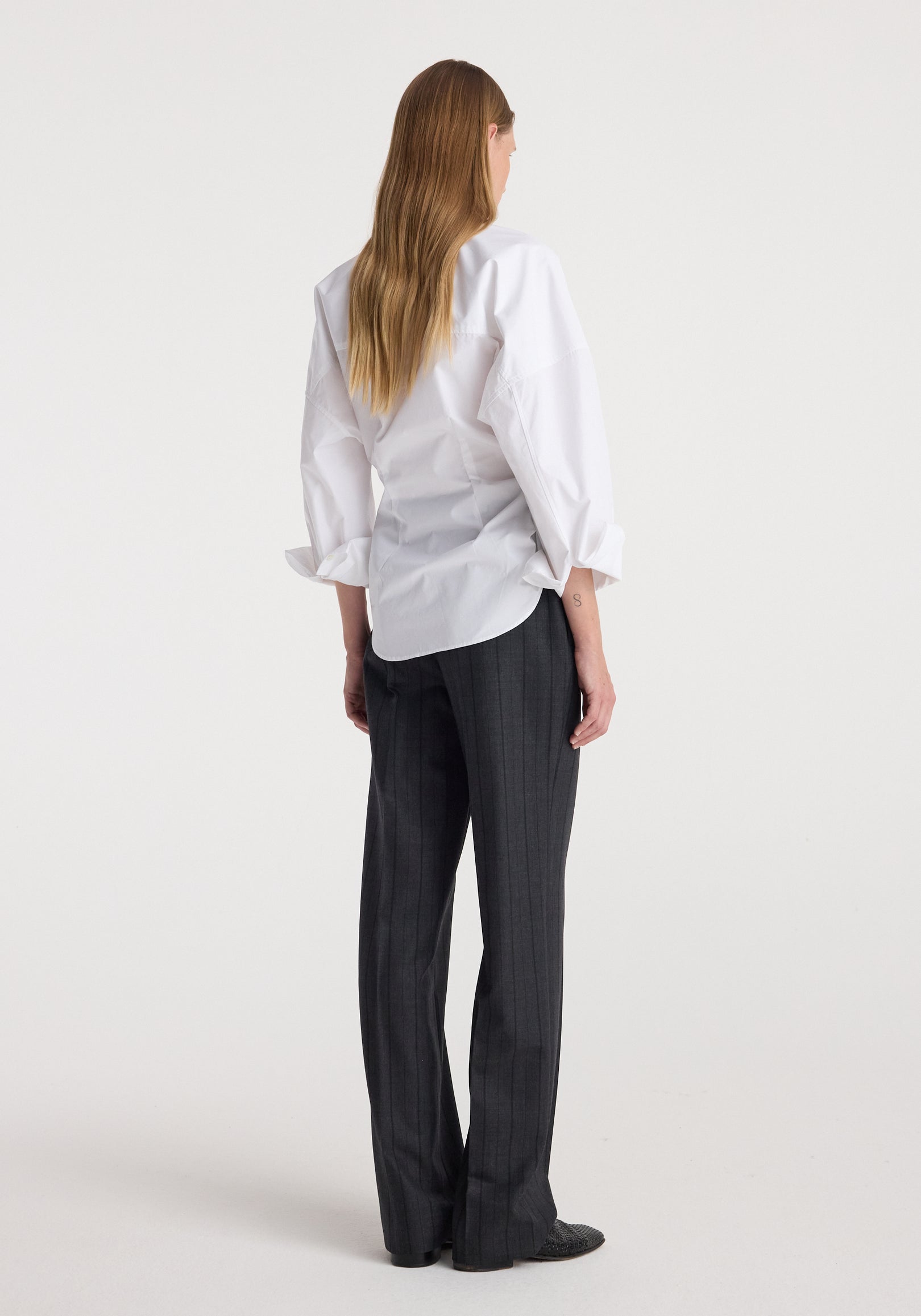 Woman wearing Kee - Straight leg tailored trousers | charcoal stripe paired with a white long-sleeve shirt, standing facing away against a plain background.
