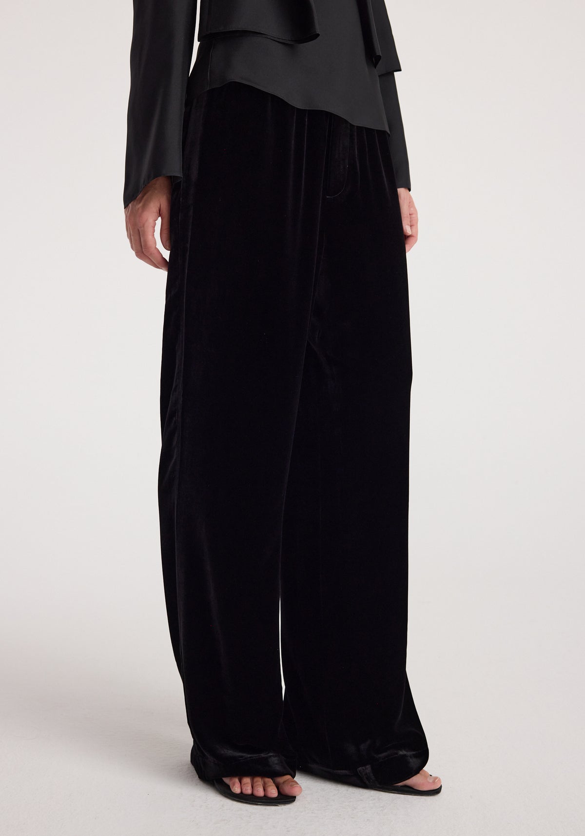 Velvet relaxed trousers | black with a loose, wide-leg fit, styled with a black long-sleeve top and open-toe sandals on a light background.