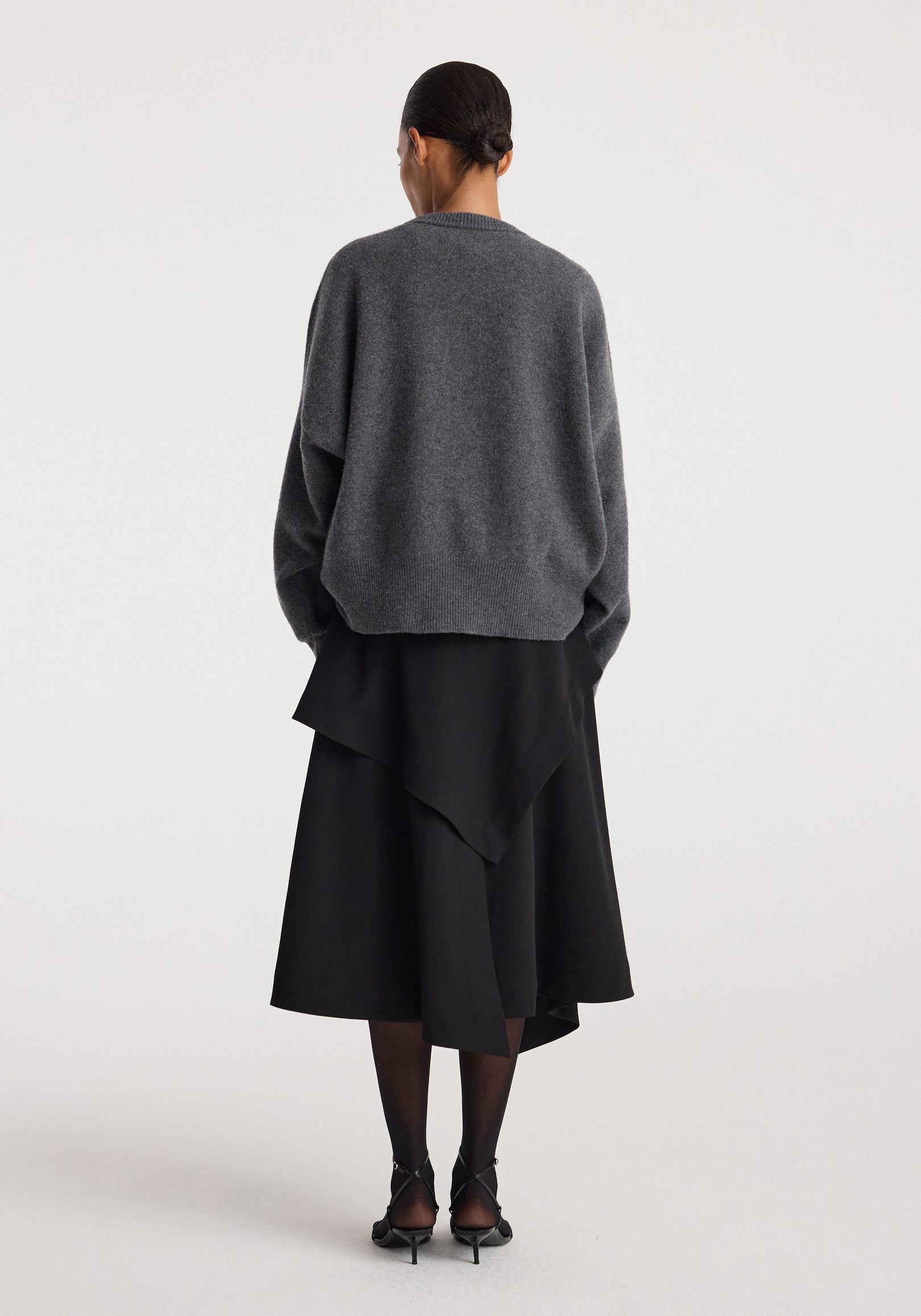 Woman wearing black layered asymmetric skirt with an oversized dark gray sweater and black heels, showcasing the back view of the Deconstructed trench skirt | black.