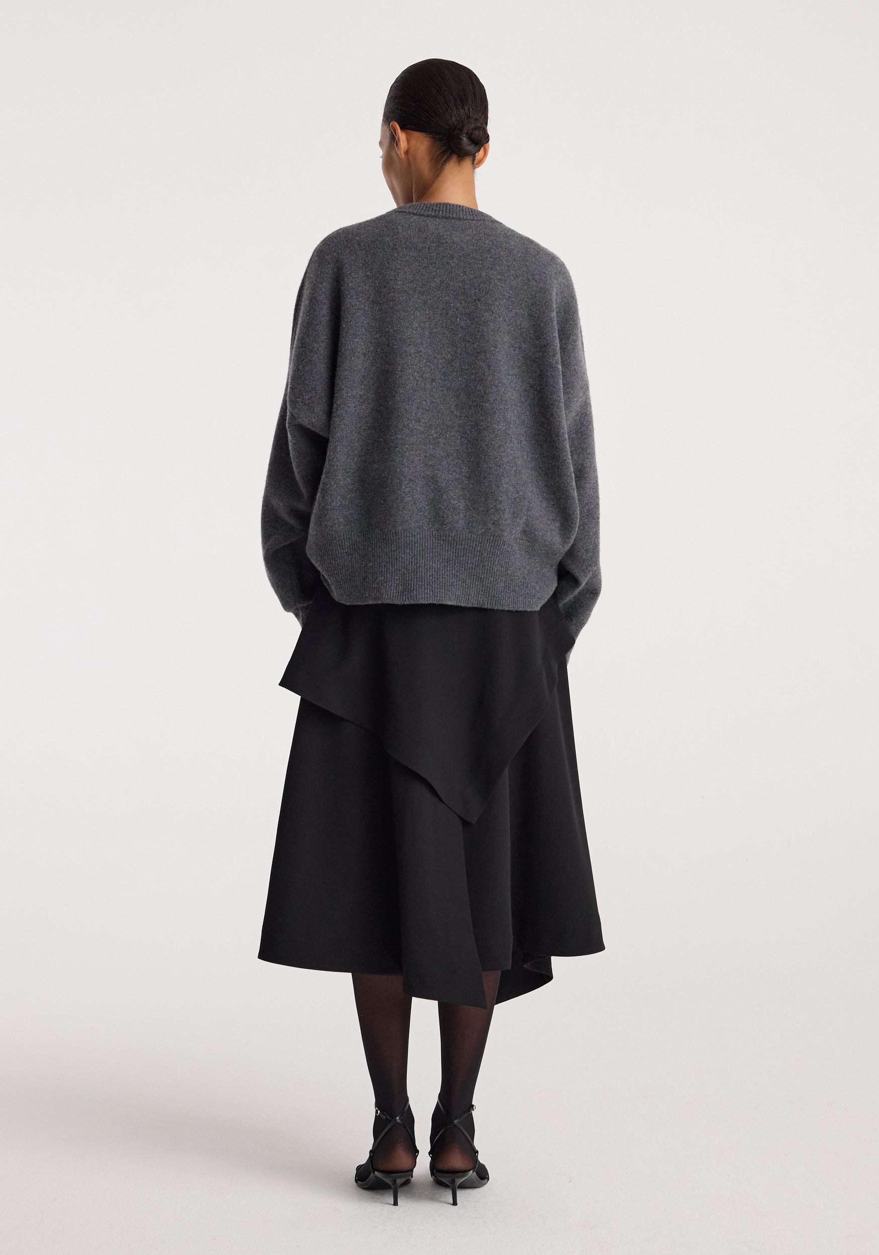 Woman wearing black layered asymmetric skirt with an oversized dark gray sweater and black heels, showcasing the back view of the Deconstructed trench skirt | black.