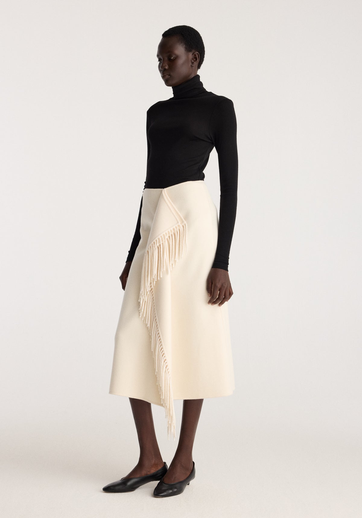 Double-faced fringe skirt | off white worn with a black turtleneck and pointed flats, featuring long draped fringe and an elegant midi silhouette
