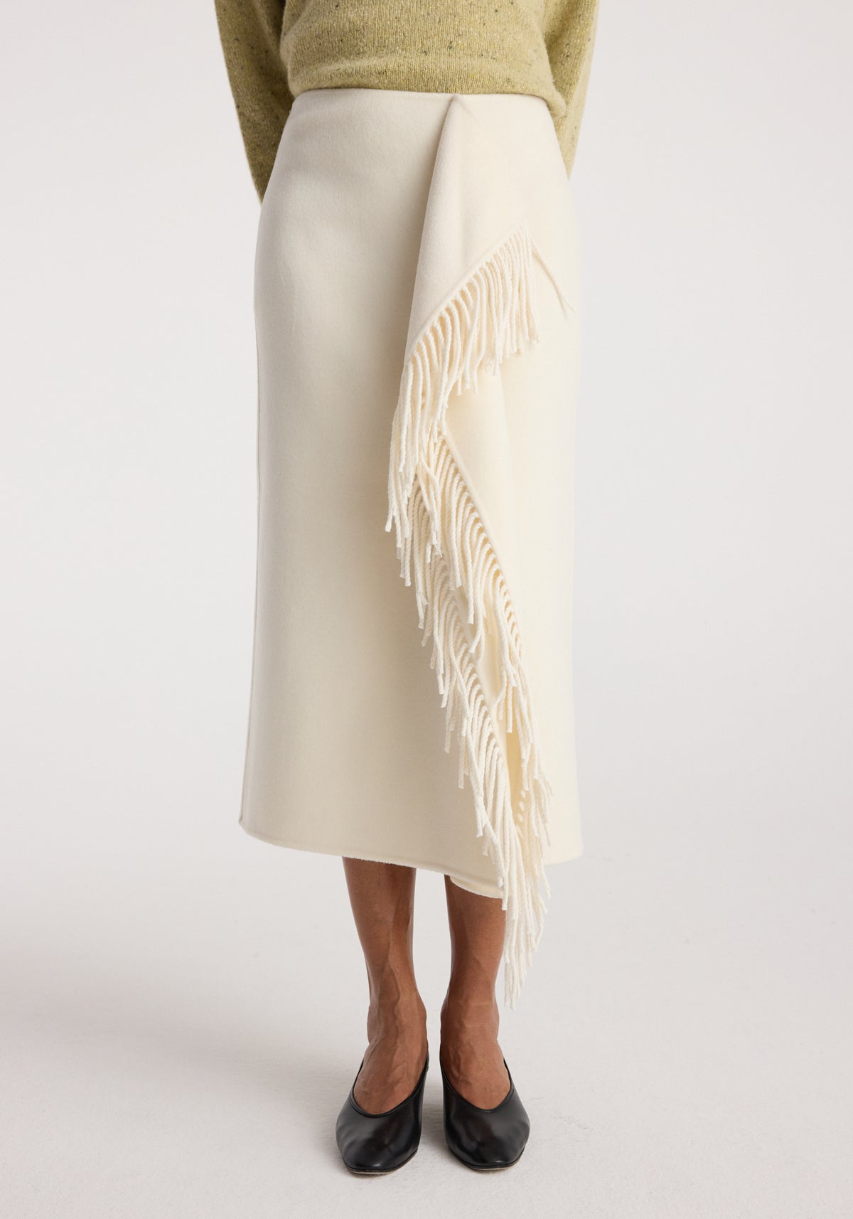 Model wearing a sophisticated double-faced fringe skirt | off white, featuring a clean, midi-length silhouette with cascading fringe detail along one side, paired with black flats.