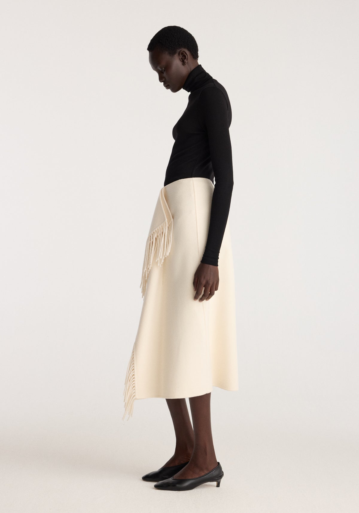 Double-faced fringe skirt | off white worn by a model with a black fitted top and pointed black heels, featuring long fringe detailing and a midi length