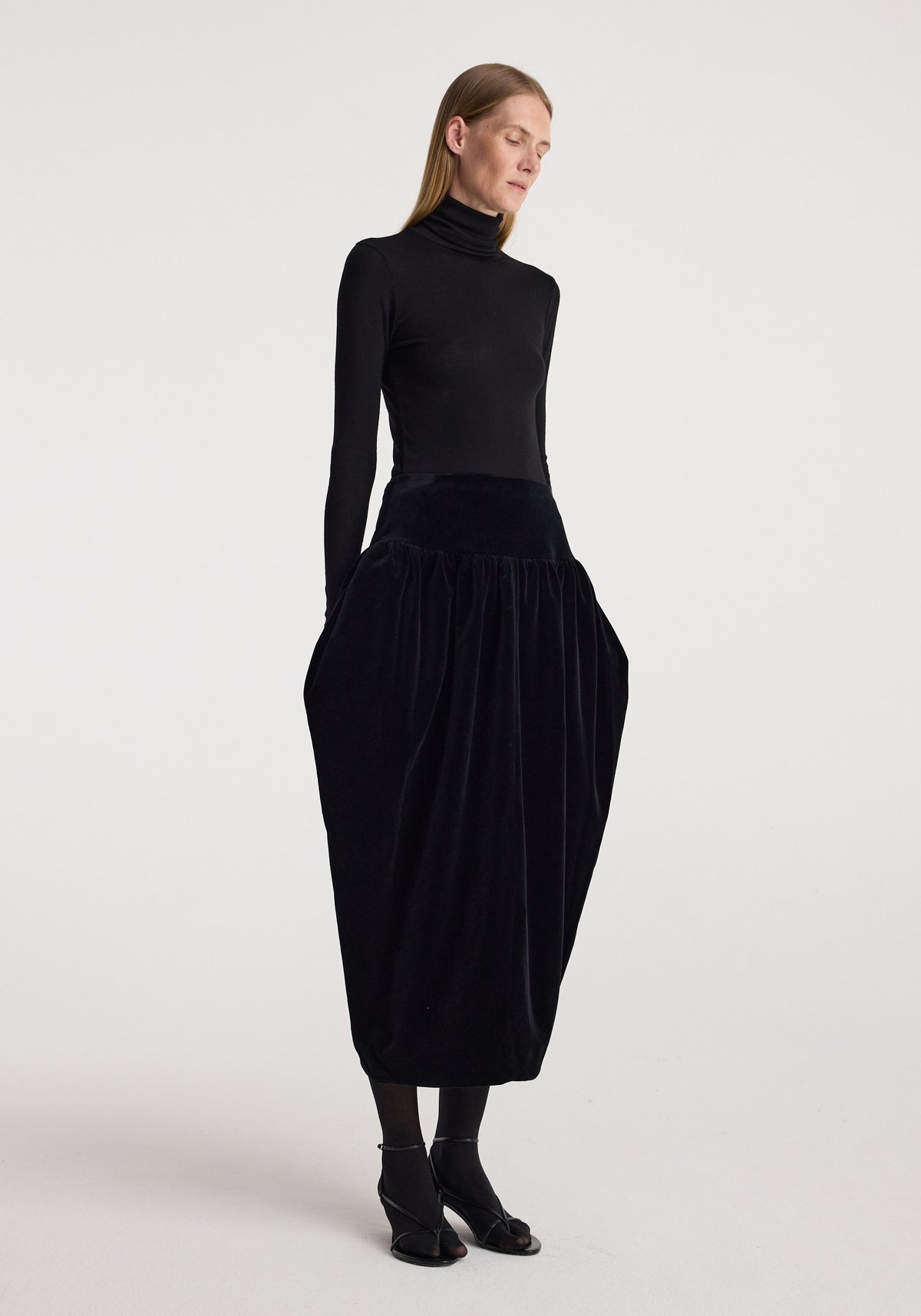 Sculptural volume velvet skirt | black worn by a model with a fitted black turtleneck and ankle boots, showcasing its dramatic gathered silhouette and full length