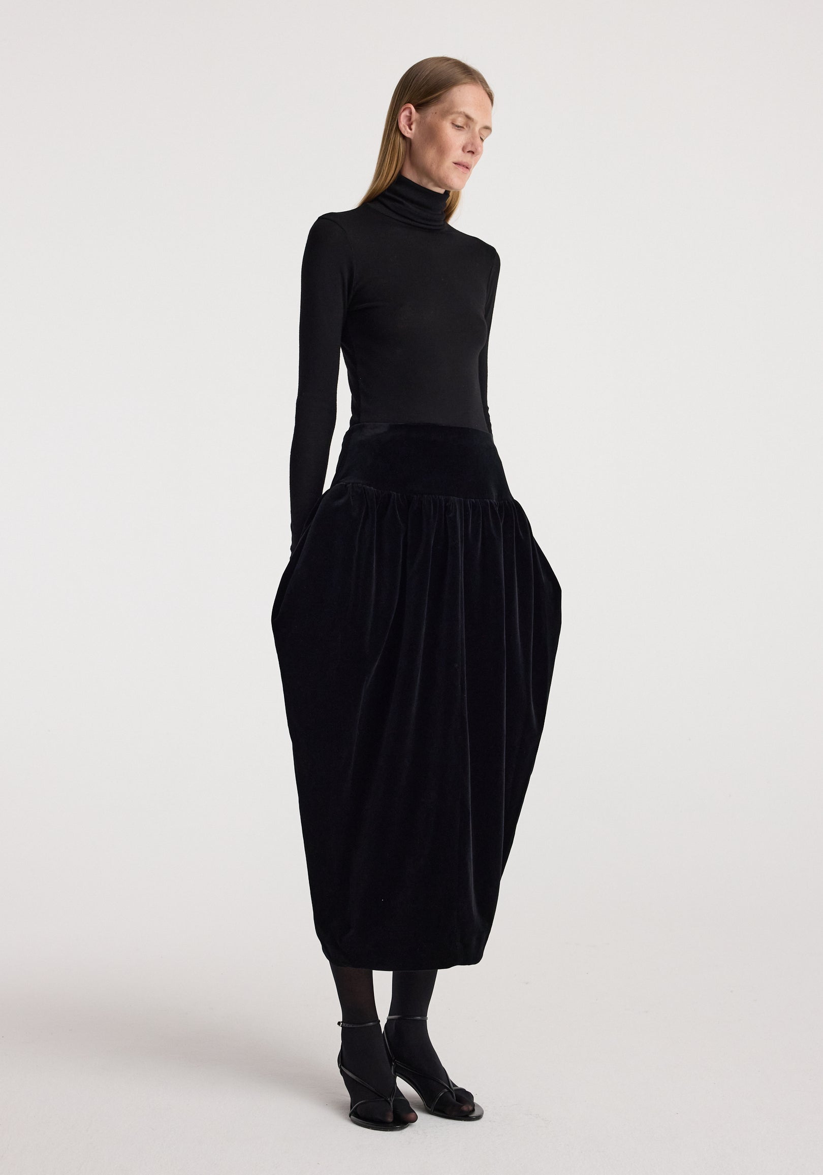 Sculptural volume velvet skirt | black worn by a model with a fitted black turtleneck and ankle boots, showcasing its dramatic gathered silhouette and full length