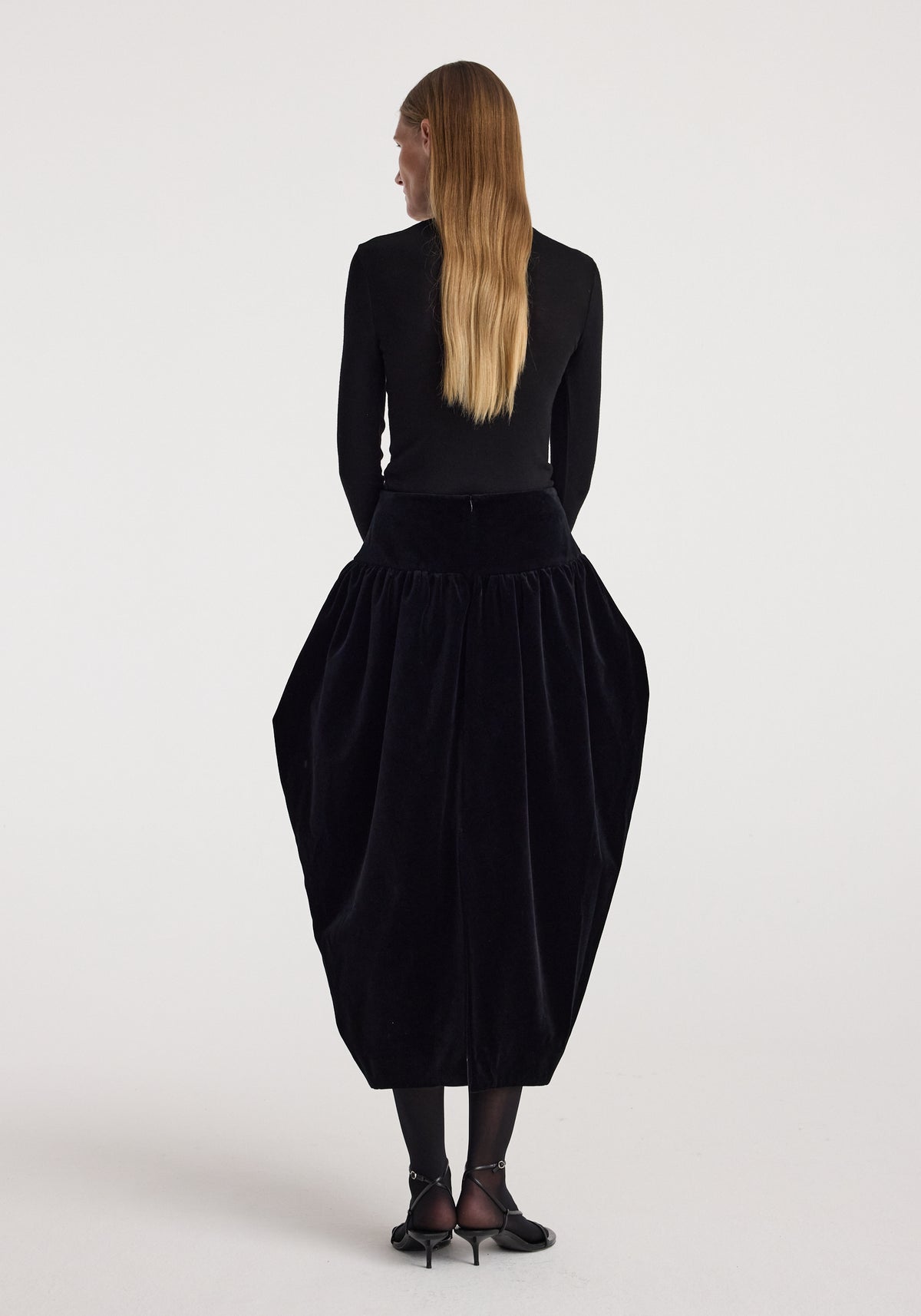 Back view of a model wearing the Sculptural volume velvet skirt | black, featuring a dramatic rounded silhouette and gathered velvet texture.