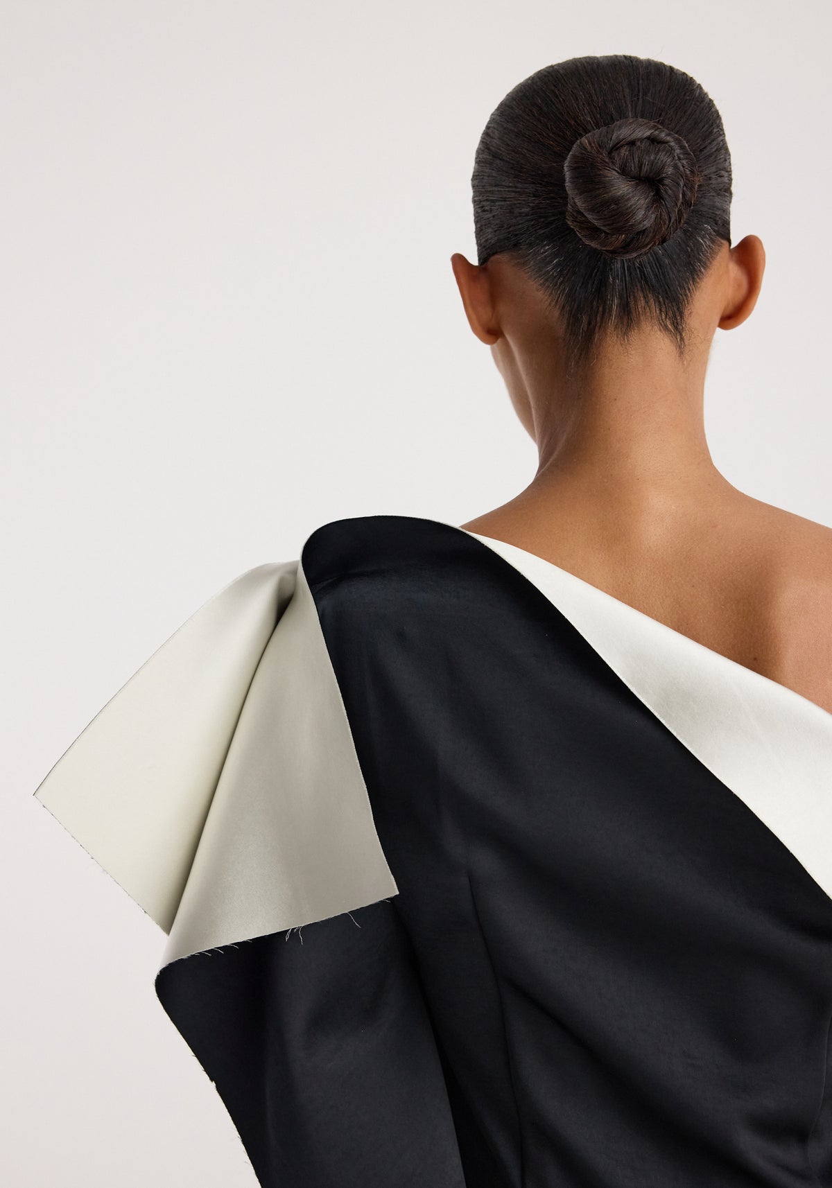 Rear view of a model wearing the sculptural double-satin off-shoulder dress | black/white, showcasing the dress's contrasting black and white fabric and elegant off-shoulder design.