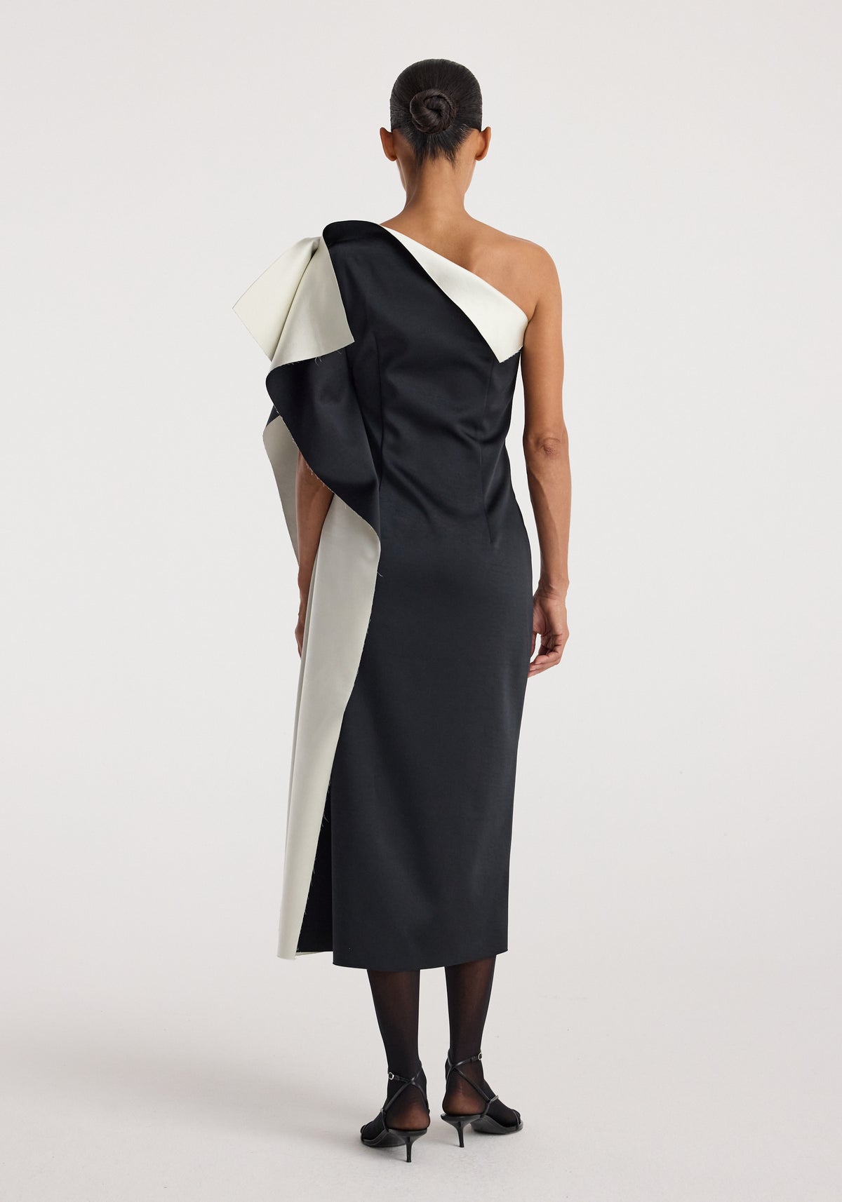 Woman seen from behind wearing a Sculptural double-satin off-shoulder dress | black/white with an asymmetrical design and sculptural detailing on one shoulder.