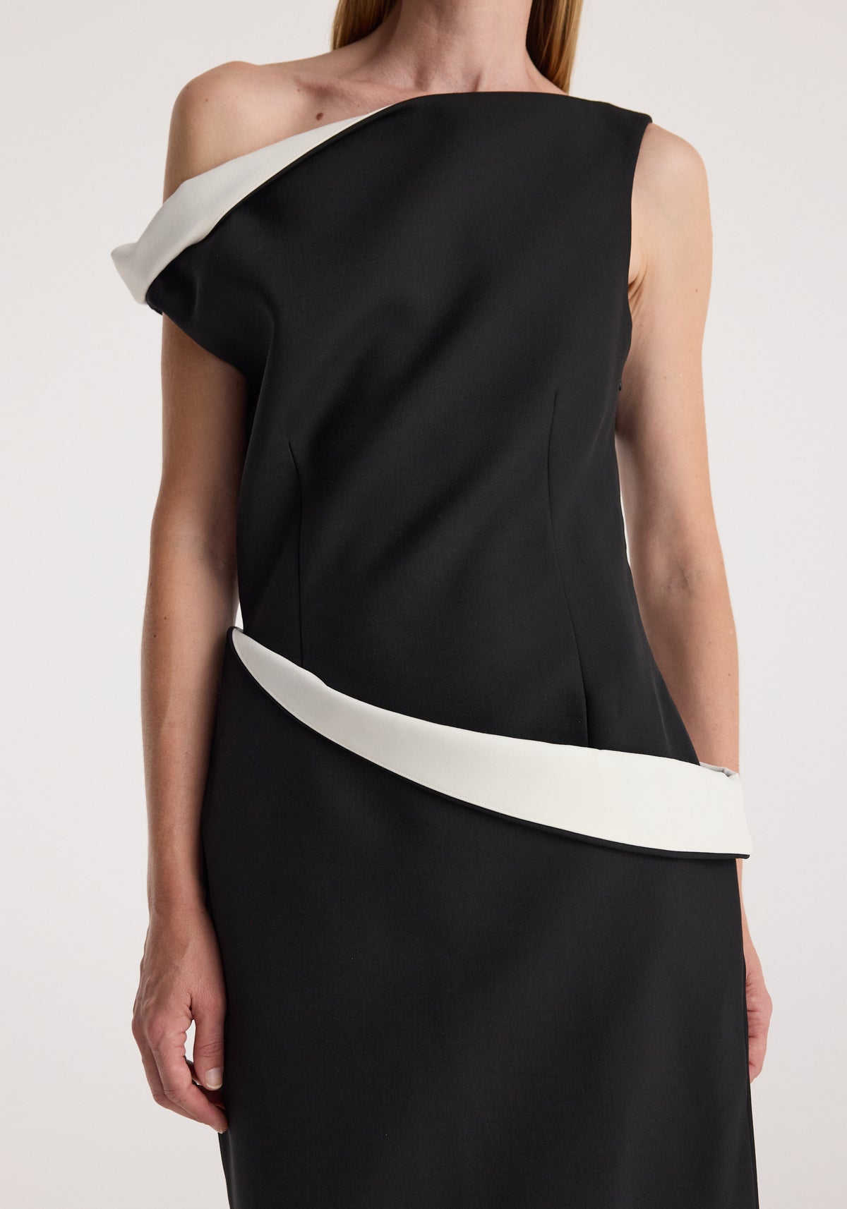 Woman wearing a Sculptural off shoulder dress | black with a unique white folded detail across the neckline and waist, showcasing a modern and elegant design.
