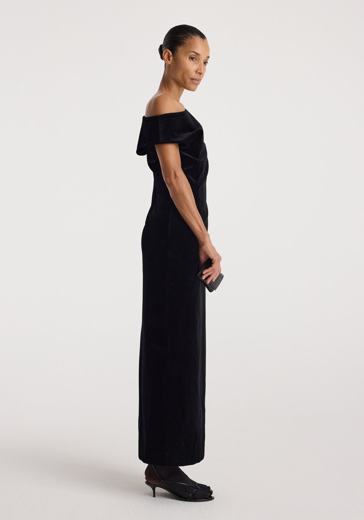 Sculptural off-shoulder velvet gown | black shown on a model in profile, featuring a floor-length silhouette and elegant draped neckline