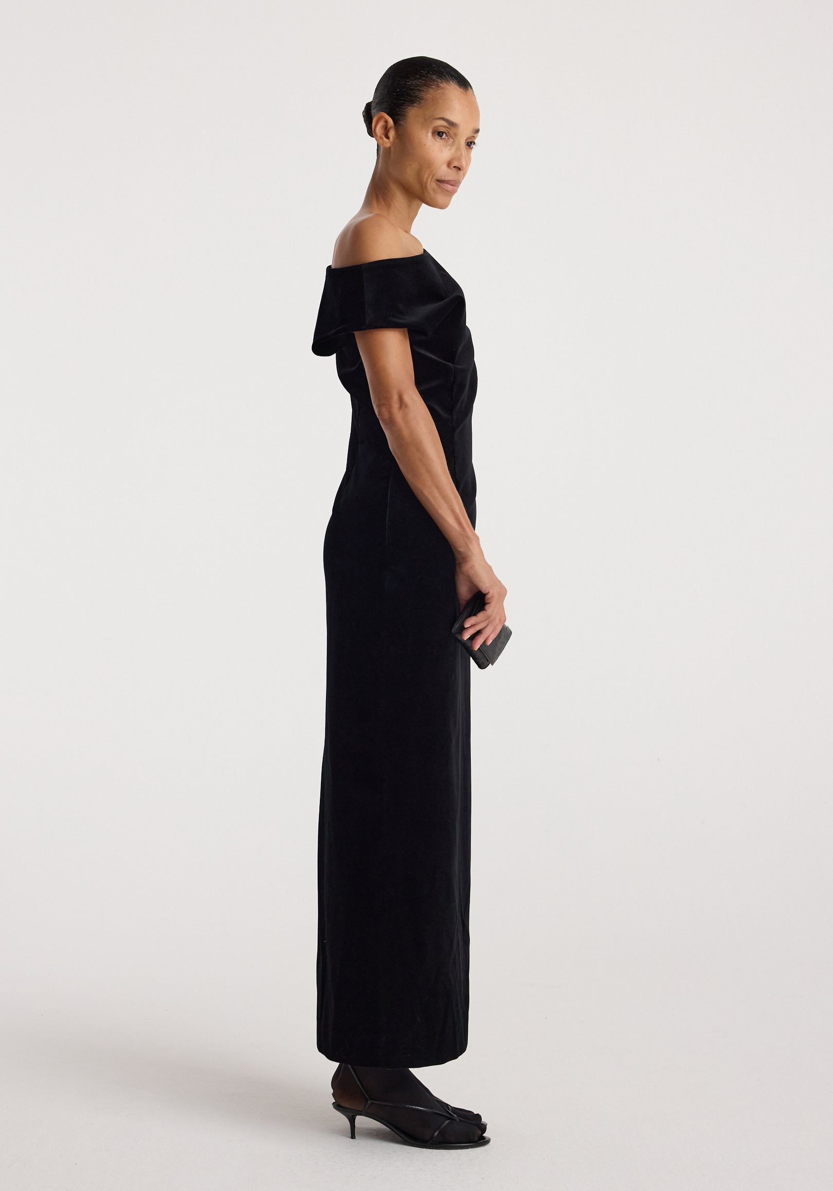 Sculptural off-shoulder velvet gown | black shown on a model in profile, featuring a floor-length silhouette and elegant draped neckline