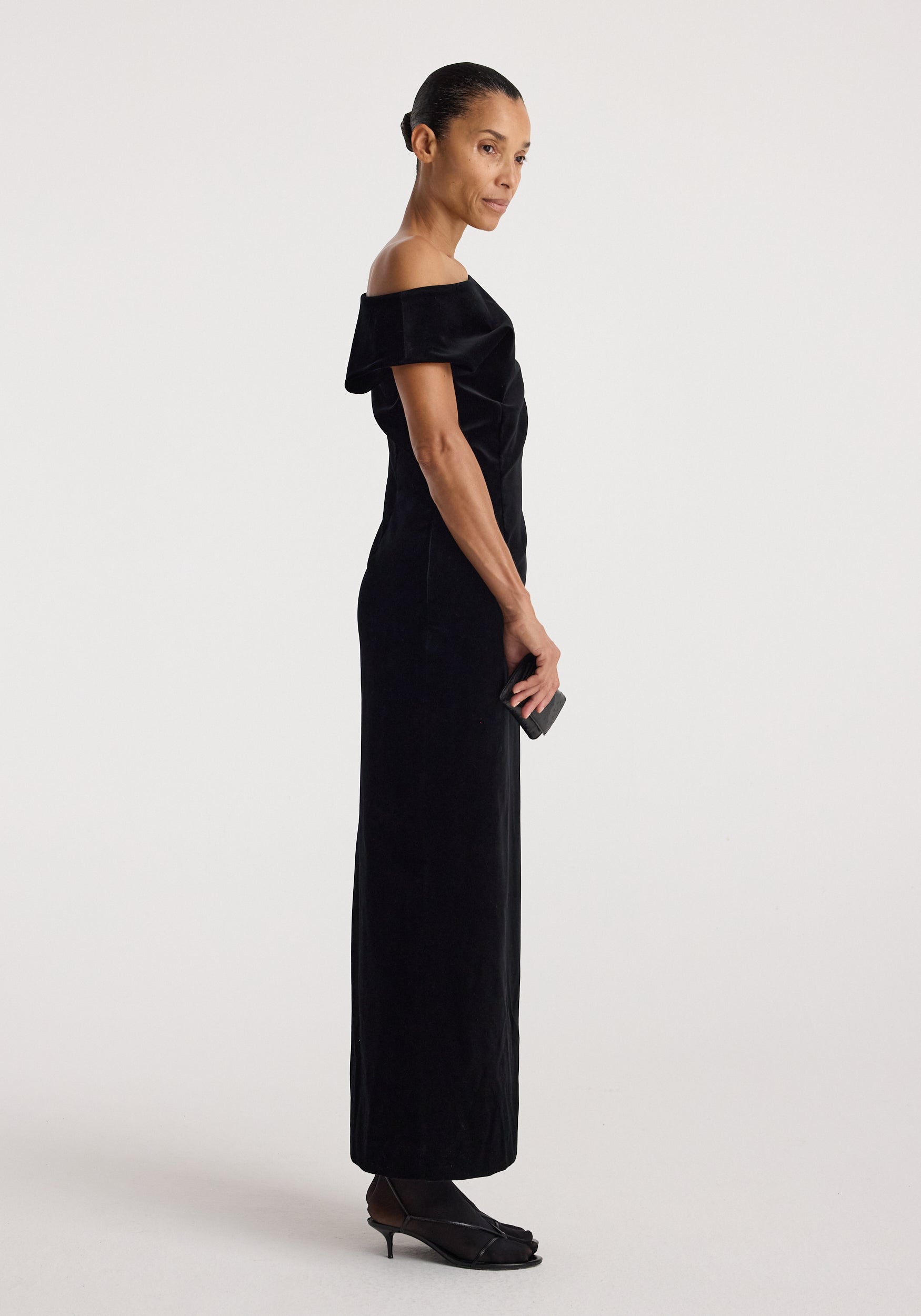 Sculptural off-shoulder velvet gown | black shown on a model in profile, featuring a floor-length silhouette and elegant draped neckline