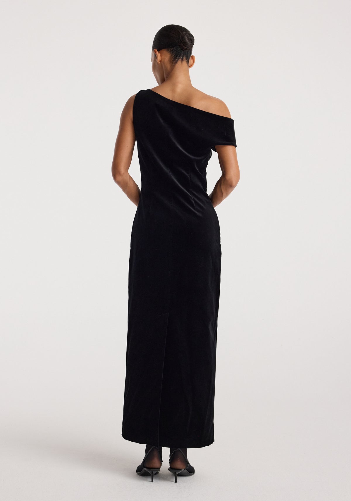 Back view of a model wearing the Sculptural off-shoulder velvet gown | black, featuring an elegant draped neckline and floor-length silhouette.