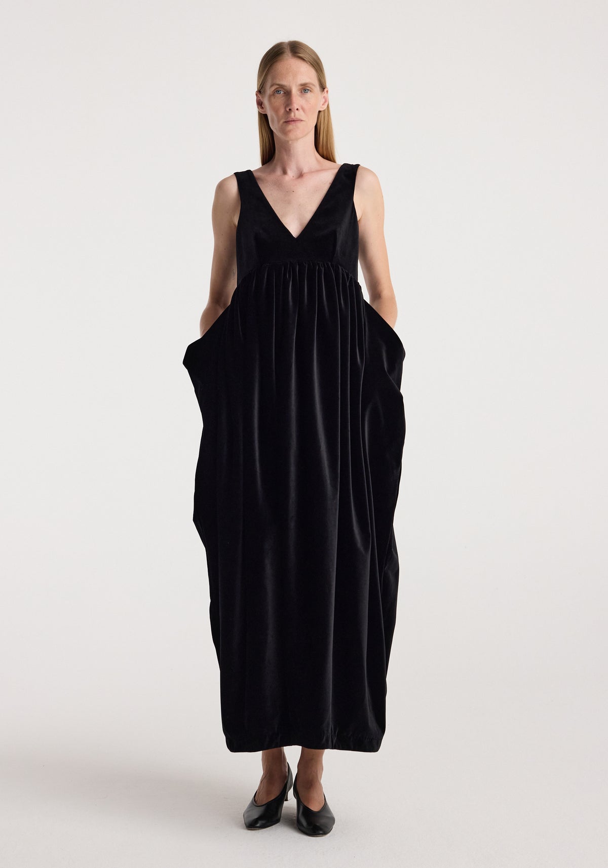 Sculptural volume velvet dress | black shown on a model, featuring a deep V neck, sleeveless design, gathered waist, voluminous silhouette, and side pockets