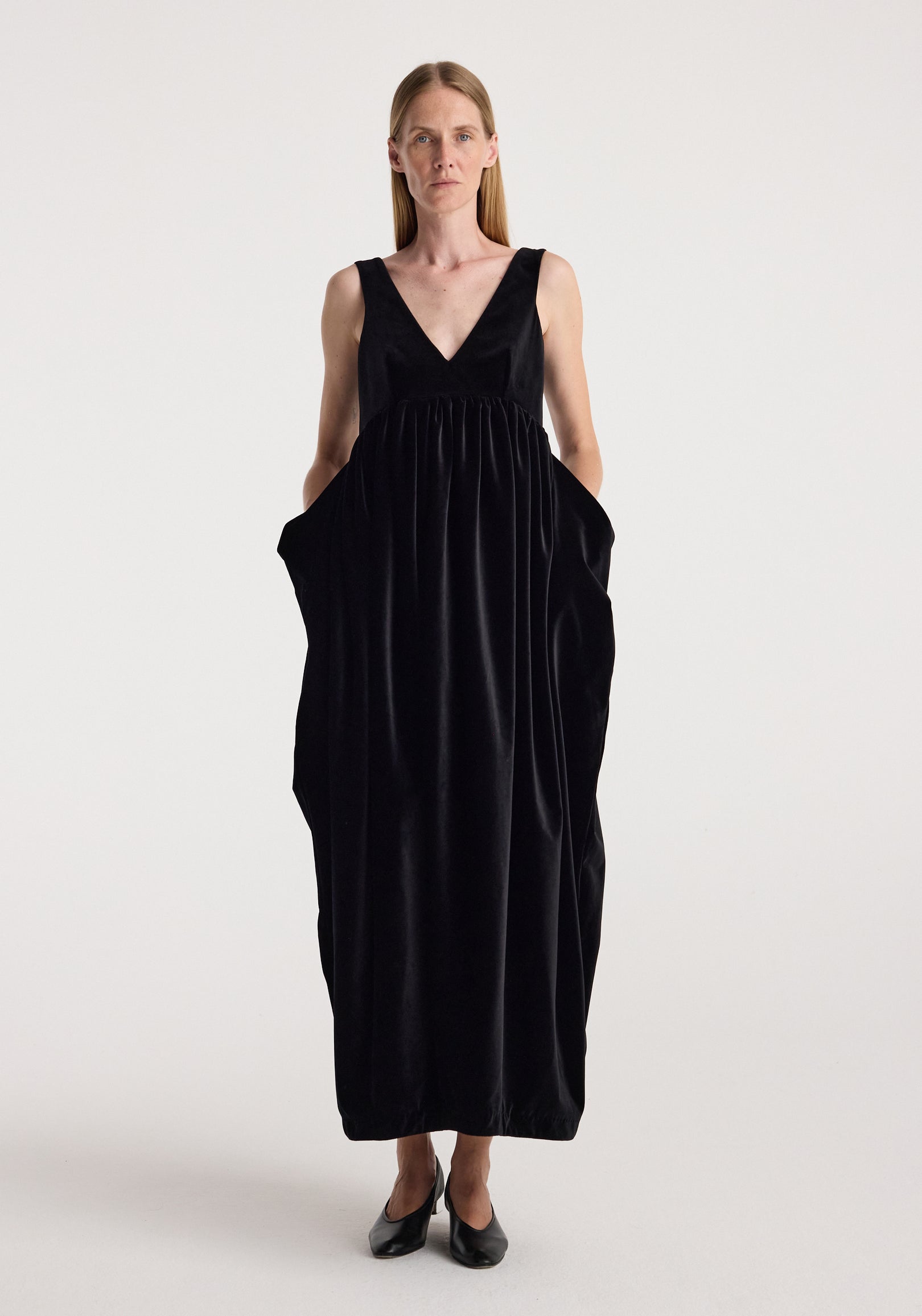 Sculptural volume velvet dress | black shown on a model, featuring a deep V neck, sleeveless design, gathered waist, voluminous silhouette, and side pockets