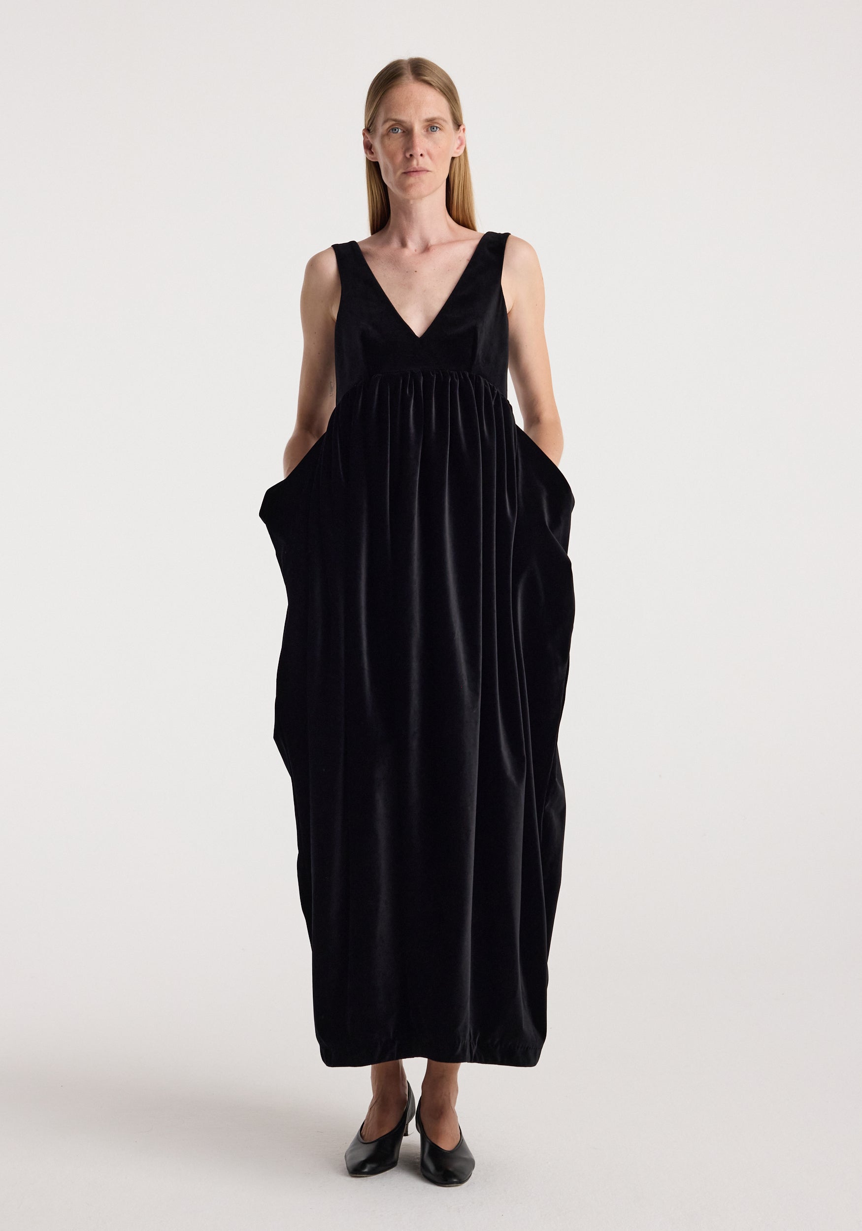 Sculptural volume velvet dress | black shown on a model, featuring a deep V neck, sleeveless design, gathered waist, voluminous silhouette, and side pockets