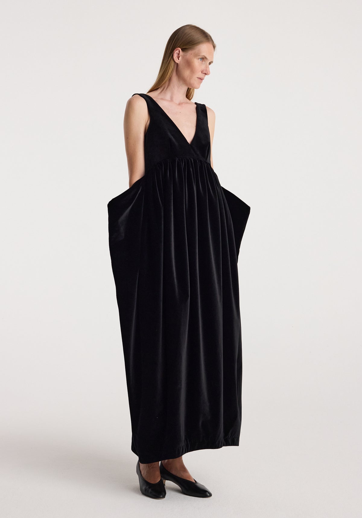 Sculptural volume velvet dress | black, worn by a woman with a deep V neckline, gathered full skirt, and black flats against a light background