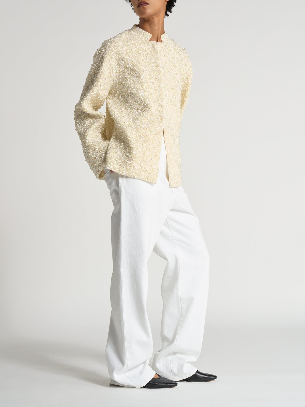 Model wearing the Hand-beaded pearl pankou jacket | pearl, a cream textured jacket styled with white trousers and black flats against a neutral studio backdrop