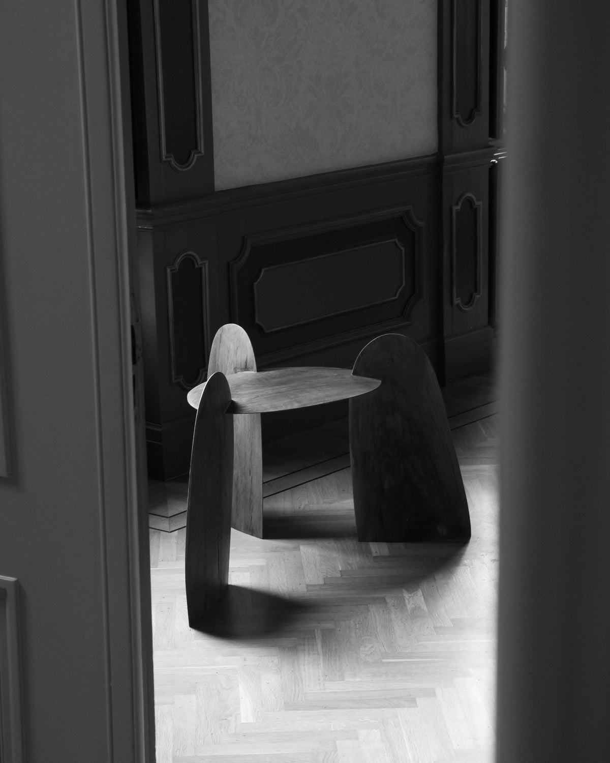 Sculpted Stool | 4673, a handcrafted oak stool by Arne Kristian, features interlocking slab legs and a triangular top, showcasing biophilic design on a parquet floor.