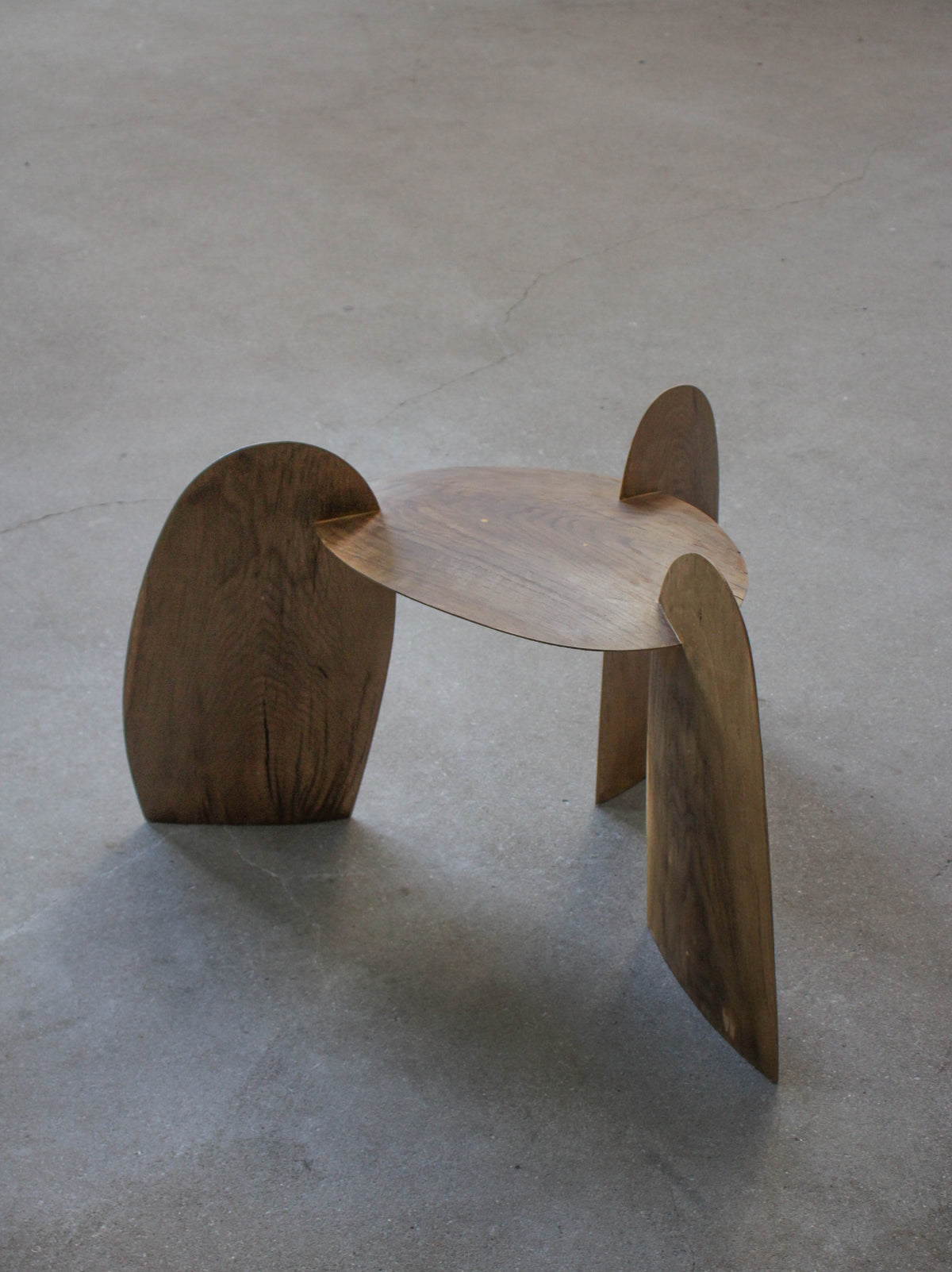 Sculpted Stool | 4673: A low, sculptural stool crafted from interlocking oak panels, forming tripod legs and a round, dished top. Handcrafted by Arne Kristian.