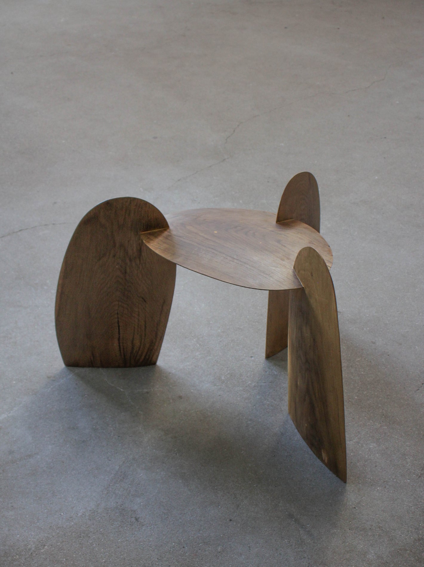 Sculpted Stool | 4673: A low, sculptural stool crafted from interlocking oak panels, forming tripod legs and a round, dished top. Handcrafted by Arne Kristian.