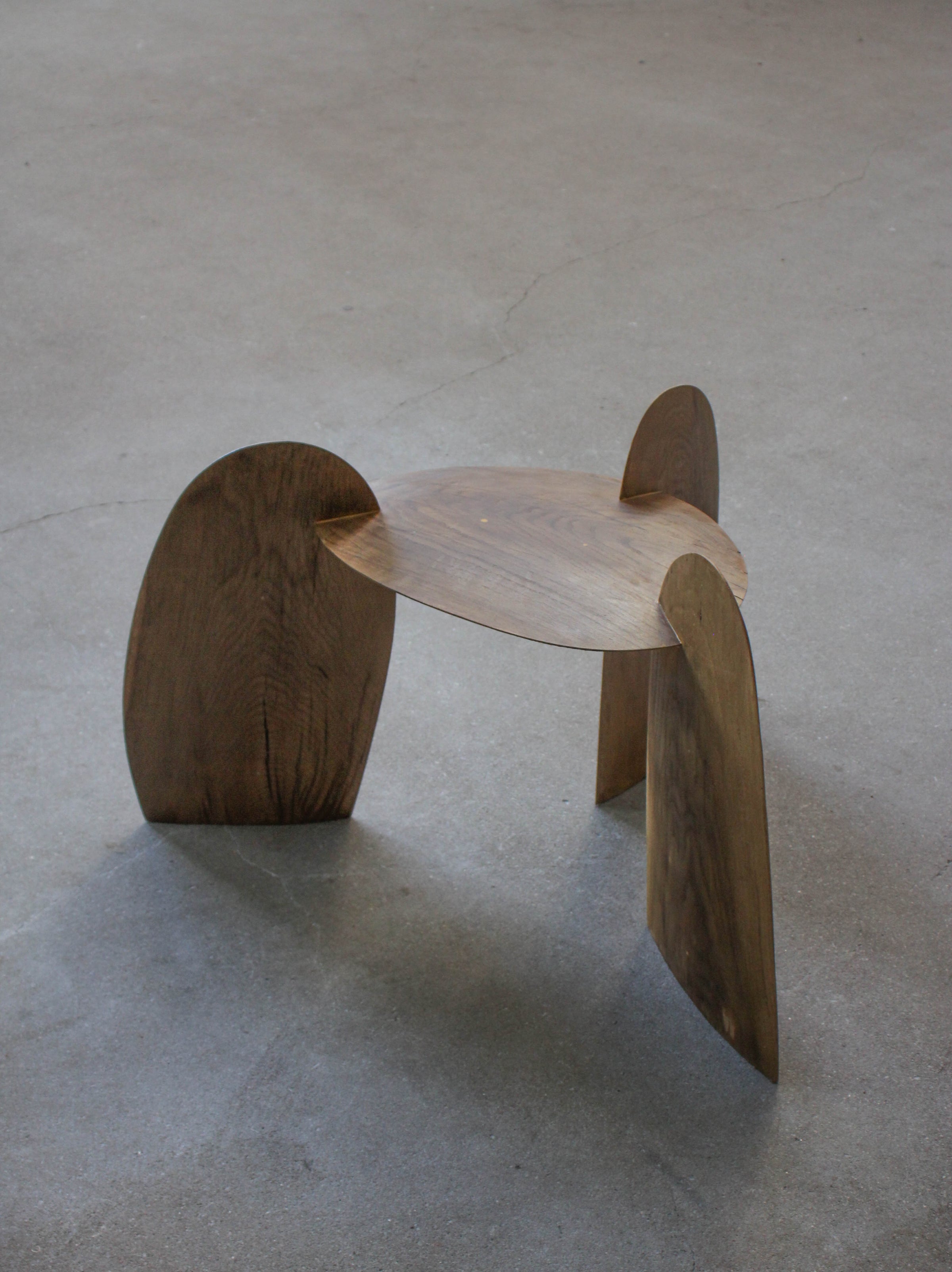 Sculpted Stool | 4673: A low, sculptural stool crafted from interlocking oak panels, forming tripod legs and a round, dished top. Handcrafted by Arne Kristian.