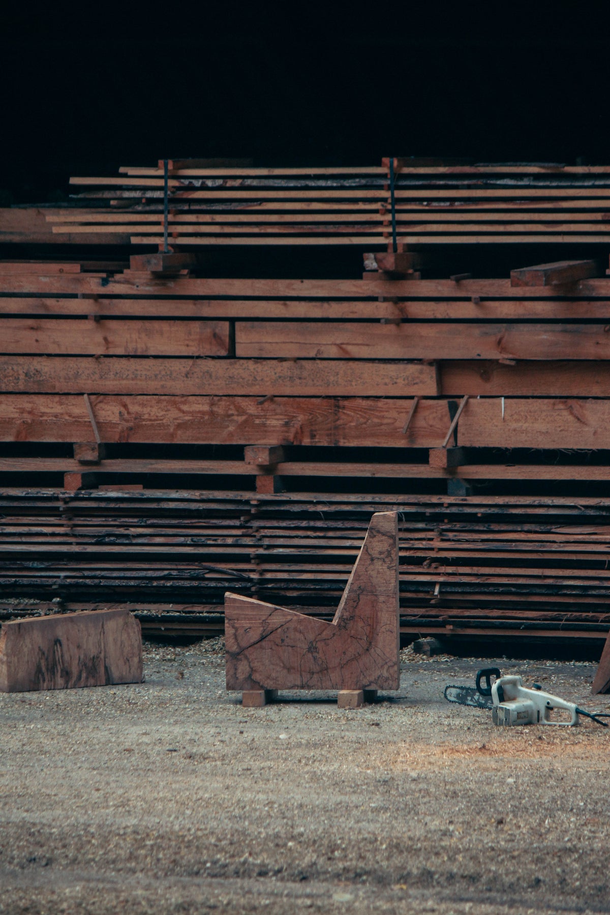 Brutalist Chair | 5788: A handcrafted oak chair featuring rough chainsaw cuts, showcasing its sculptural, functional design amidst a sawmill setting with wood planks and sawdust.